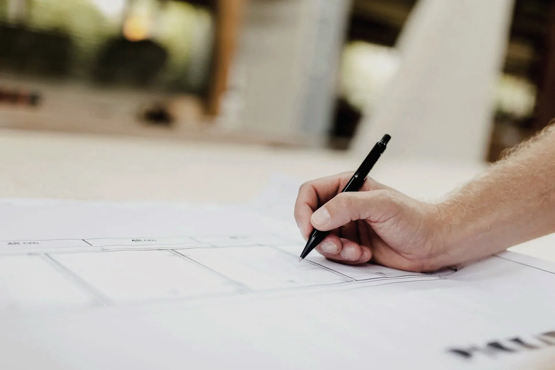 A person hand drawing on a paper with a black pen, possibly working on a blueprint or sketch.