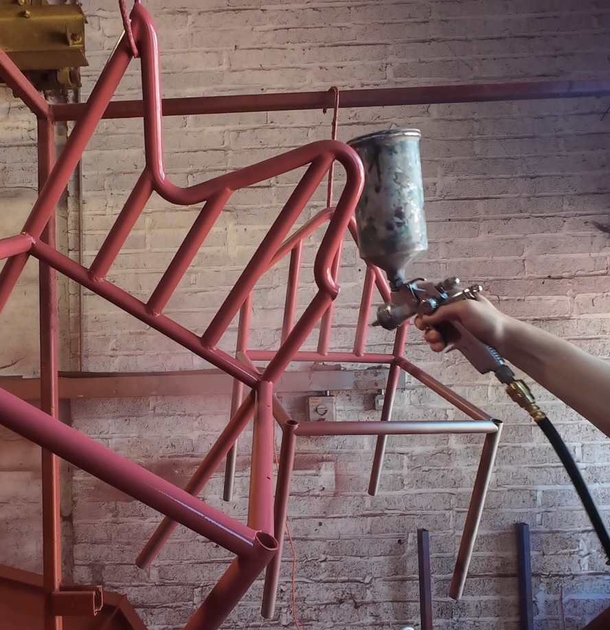 Someone spray painting a pink metal frame structure against a brick wall.