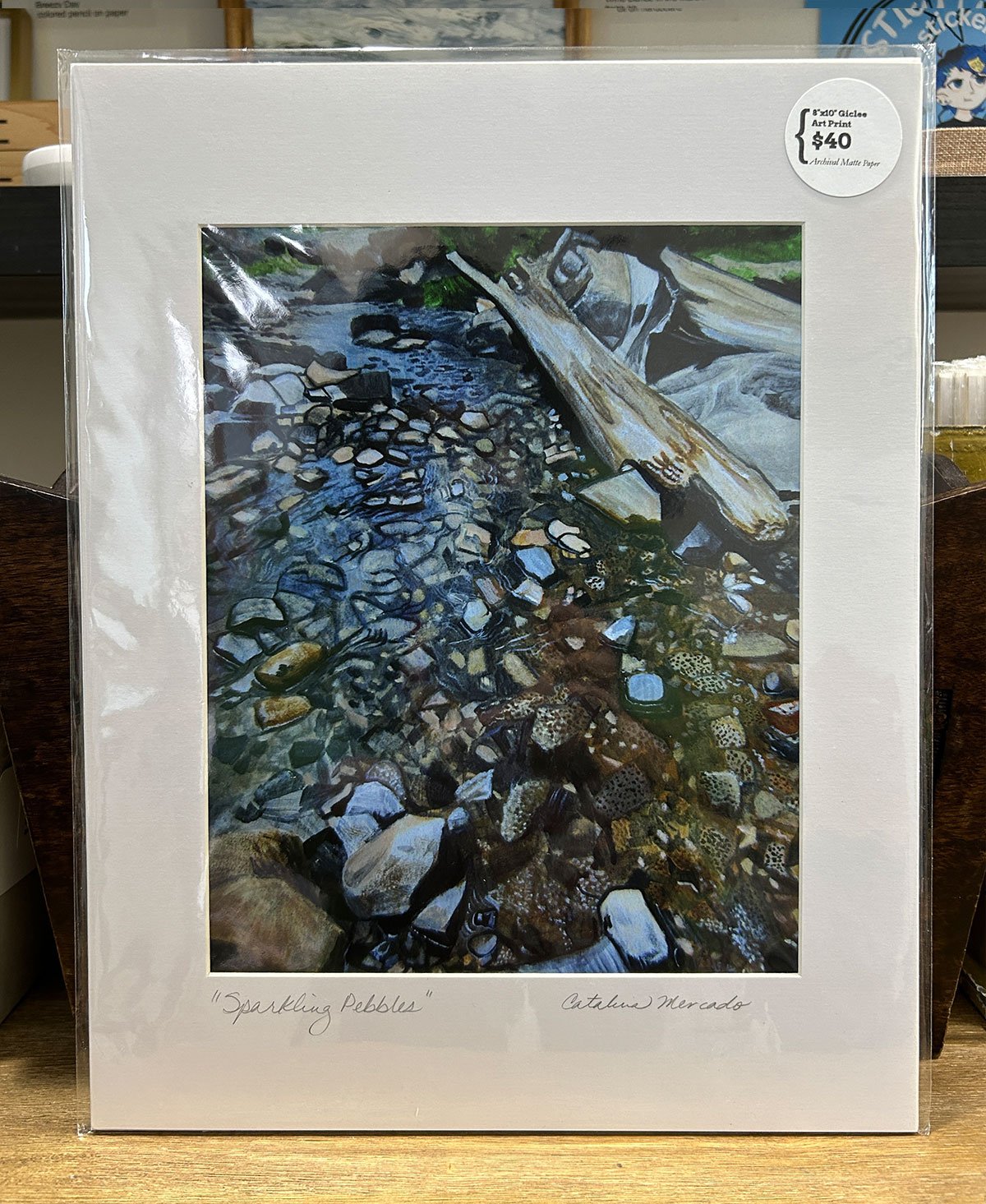 The artwork captures the natural beauty of sunlight reflecting off wet pebbles, giving them a sparkling appearance.