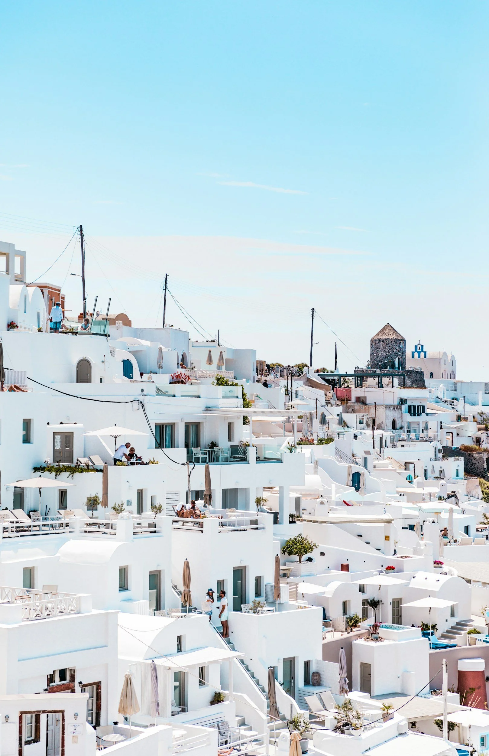 White buildings with terraces and umbrellas in a coastal town, with a clear blue sky overhead.