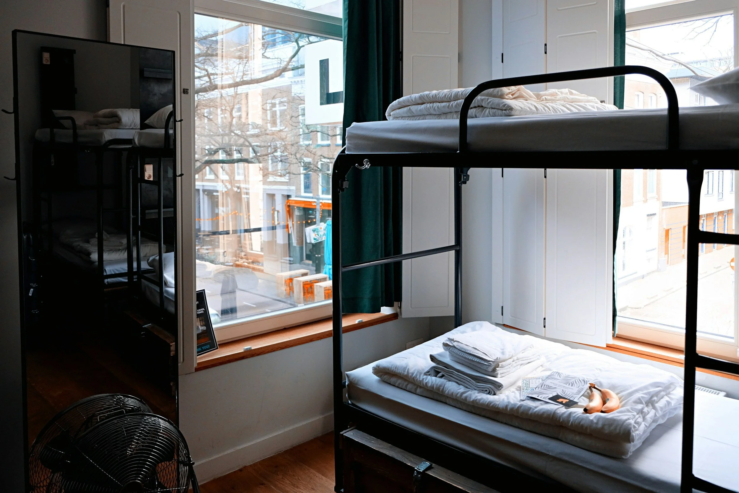 A cozy room with bunk beds and a large window showing a street scene outside, including trees and buildings.