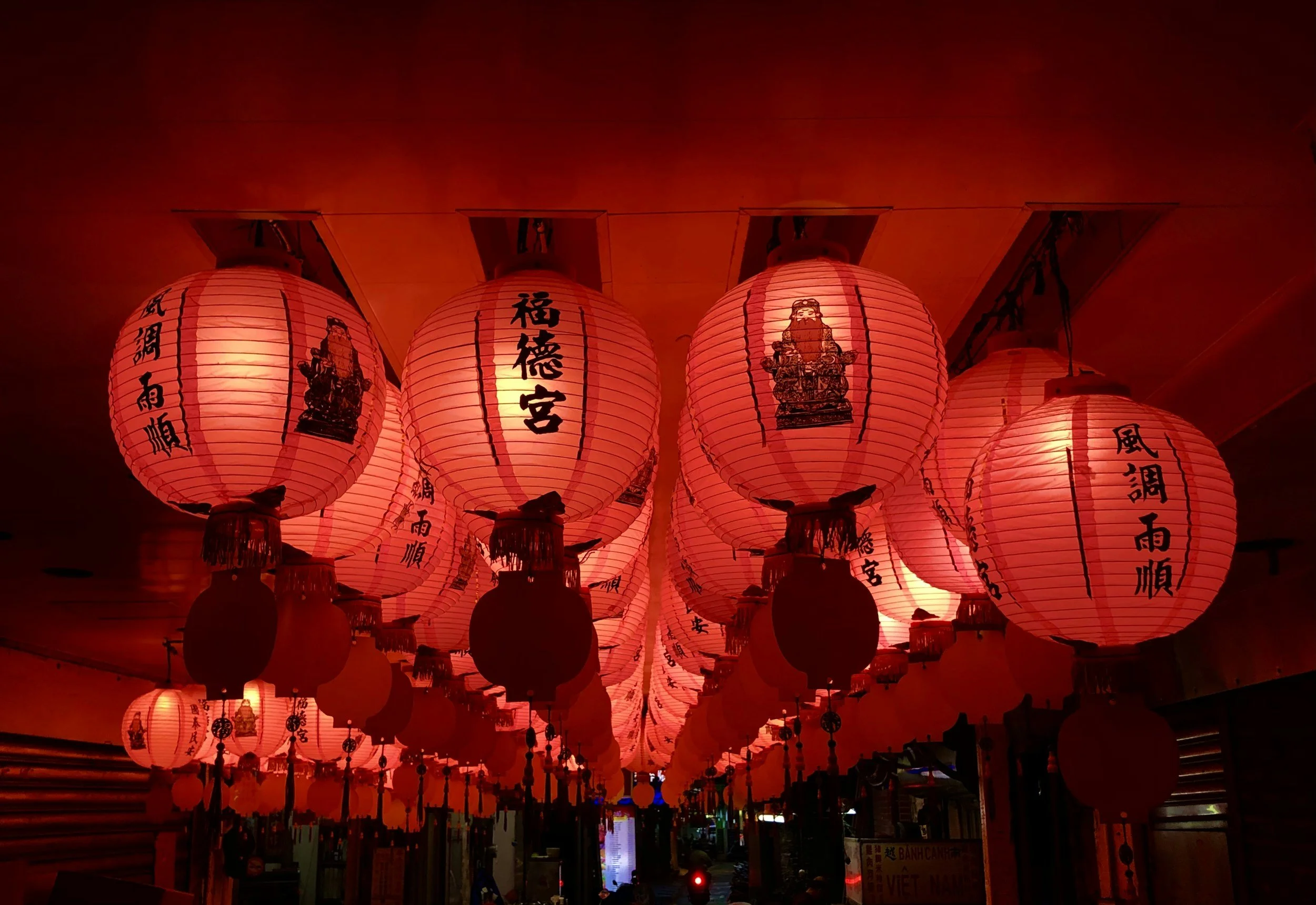 Red Chinese paper lanterns hanging from the ceiling with black Chinese characters and images of deities, creating a festive atmosphere.