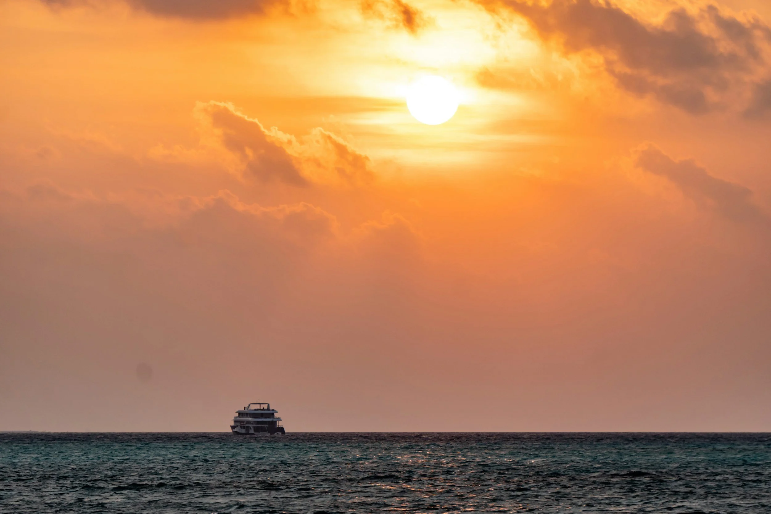 A boat on the ocean with a sunset and clouds in the sky.