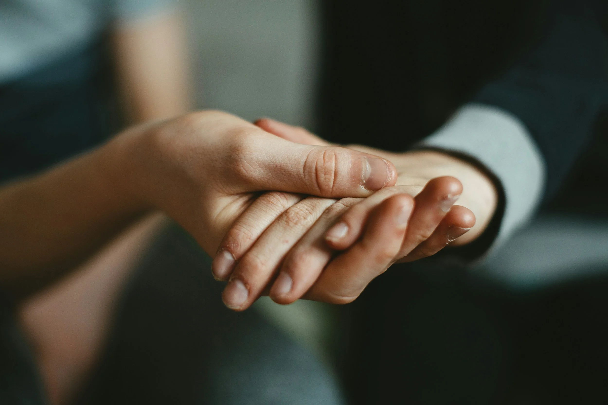 A close-up of two people holding hands, one with a lighter skin tone and the other with a darker skin tone, showing a comforting gesture.