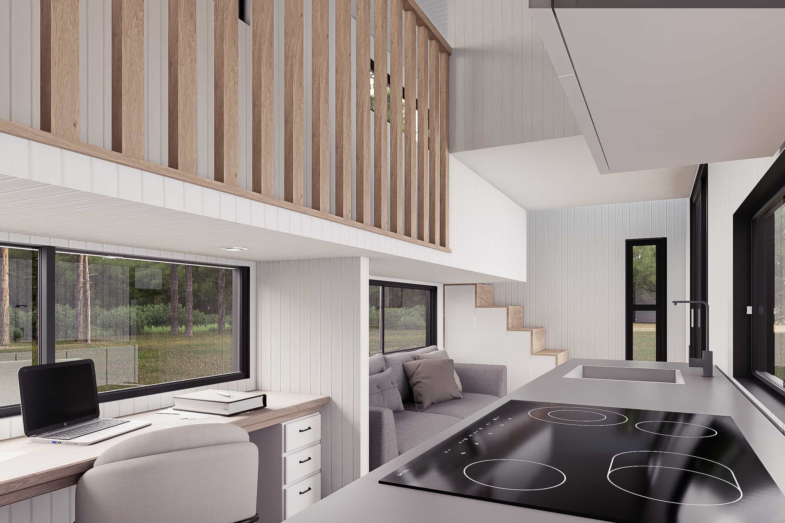 Modern open-concept living space with a kitchen area featuring an induction cooktop, a sink, and large windows overlooking a wooded outdoor area, with a small workspace including a laptop and books.