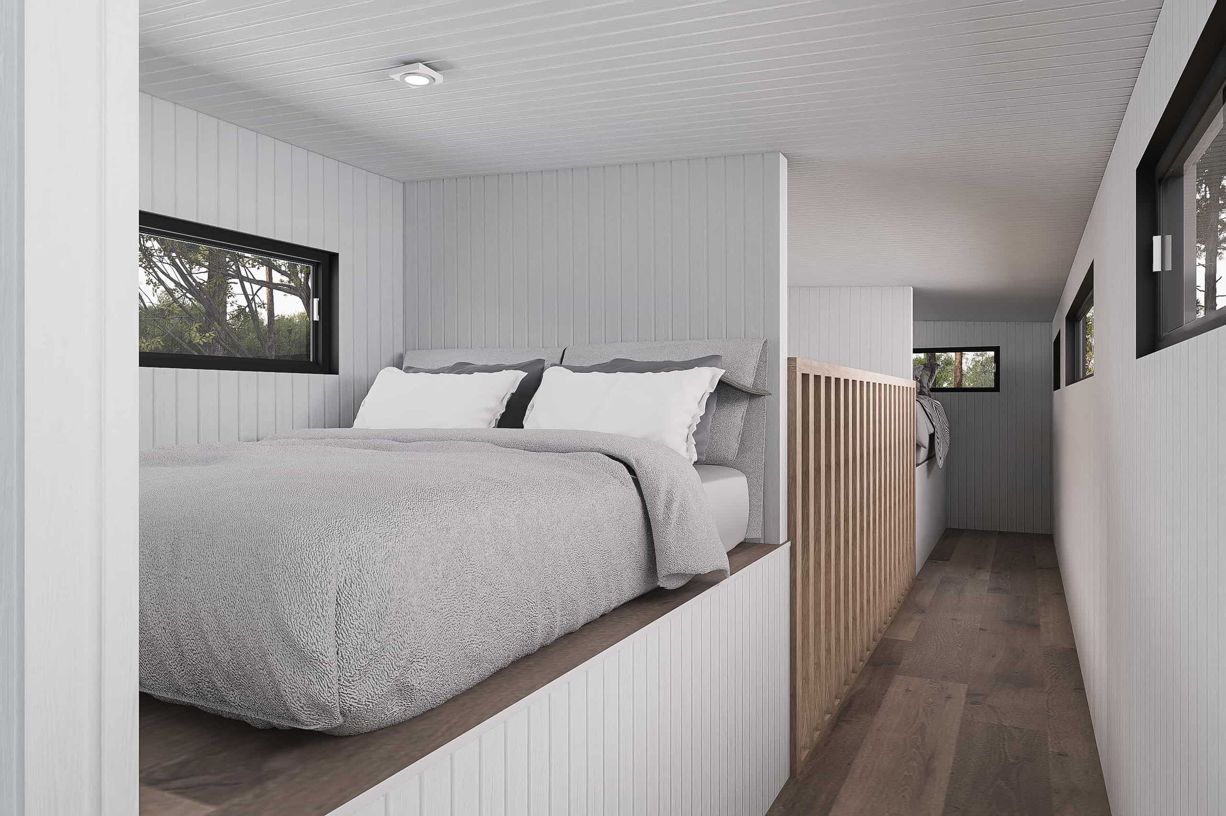 A cozy bedroom with gray bedding, white pillows, and wood accents, featuring narrow horizontal windows with trees visible outside.