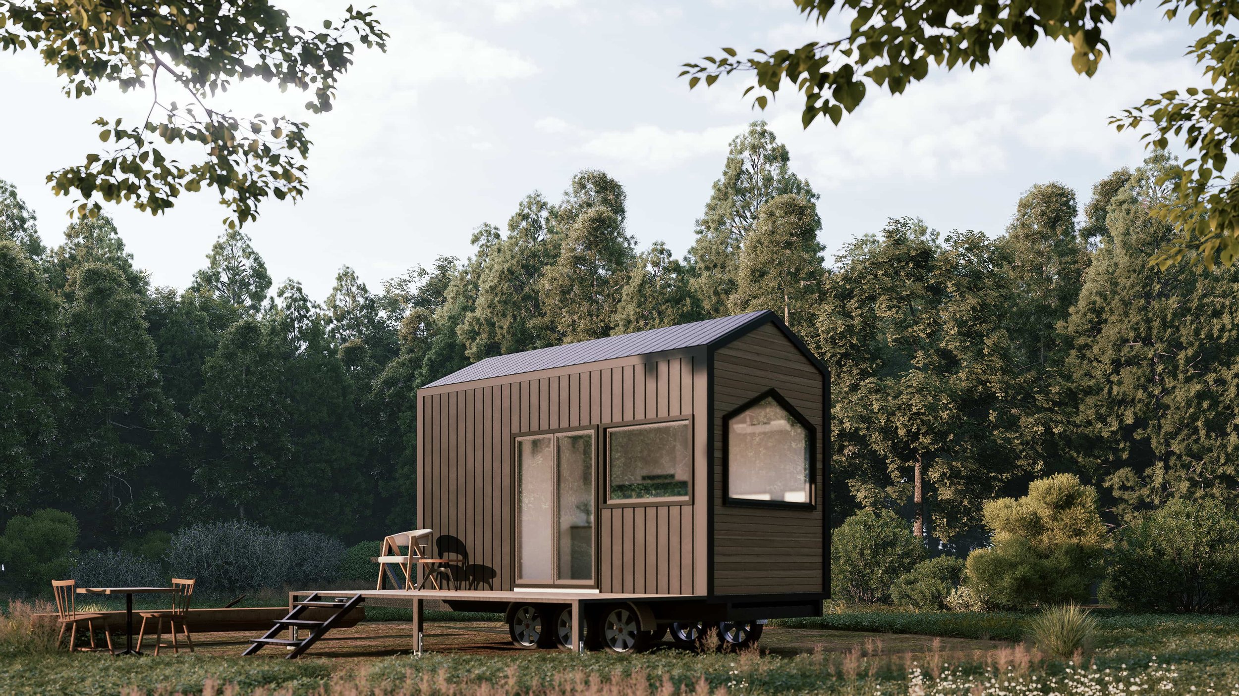 A small modern tiny house on wheels set in a lush green outdoor area with trees in the background, featuring large windows and a patio with outdoor furniture.