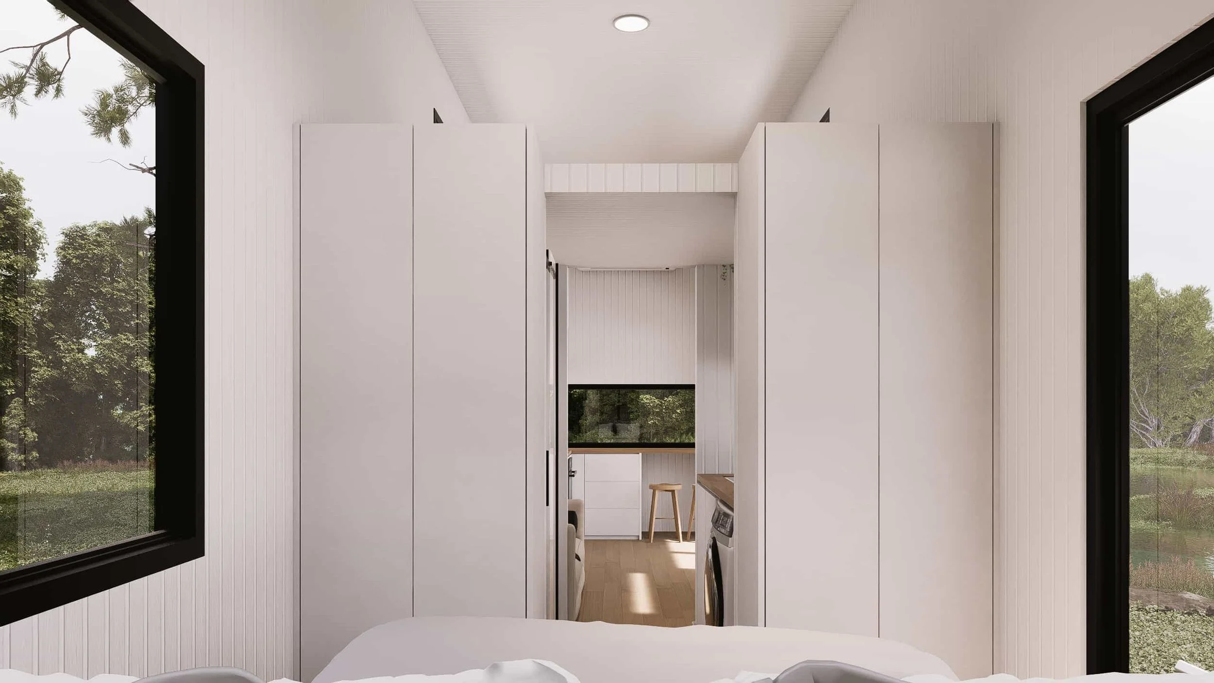 View from bedroom looking into small living area with a large window, white walls, and minimal furniture.