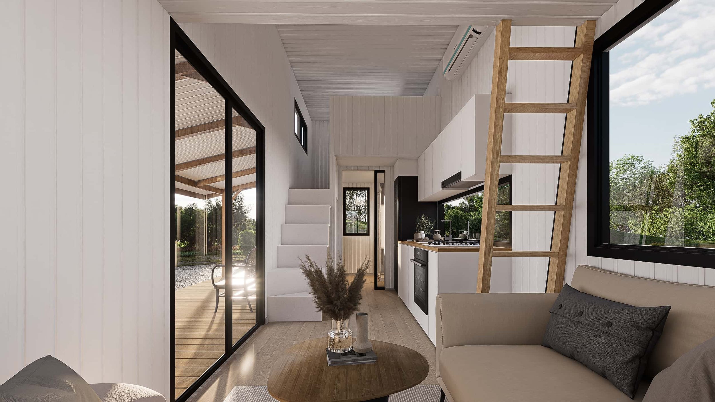Interior of a modern tiny house with a small kitchen, a beige sofa with gray pillows, a round wooden coffee table, and large windows showing outdoor greenery.