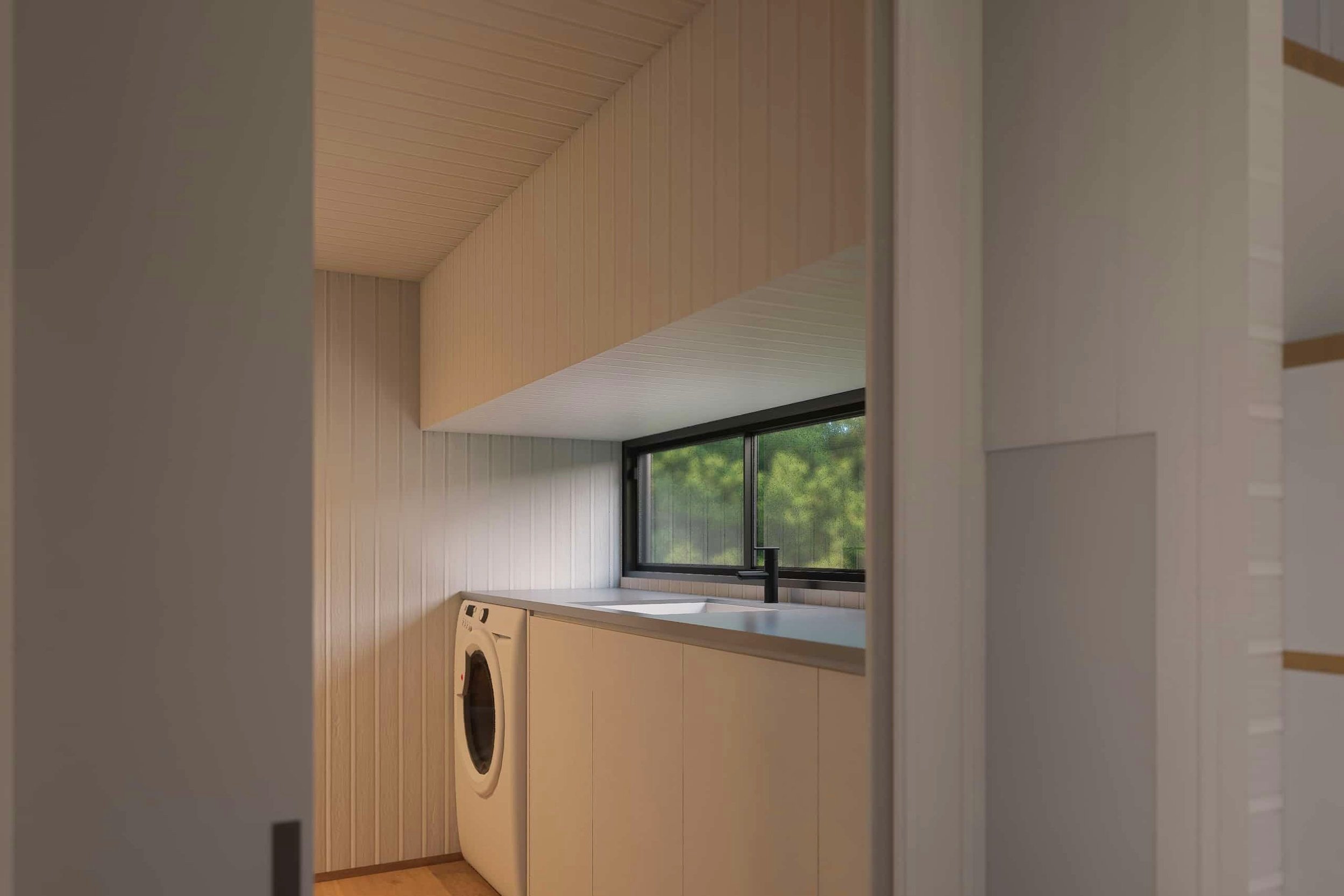 Laundry room with a front-loading washing machine, beige cabinets, and a black-framed window overlooking green trees.