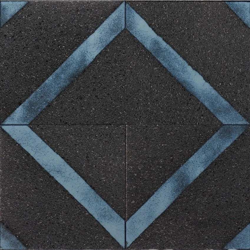 Close-up of a black rubber sidewalk tile with a blue painted diamond shape in the center, formed by four tiles.