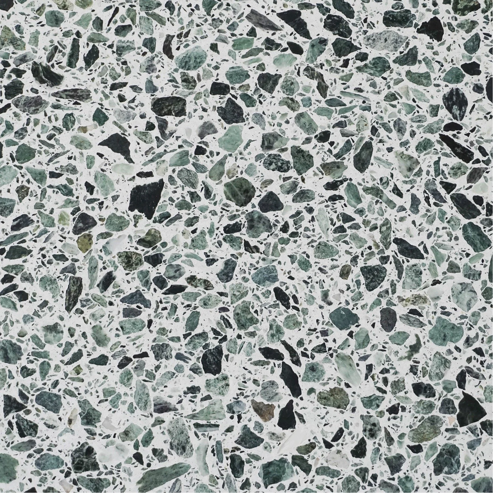 Close-up of a terrazzo floor with green, black, and gray marble chips embedded in white concrete.