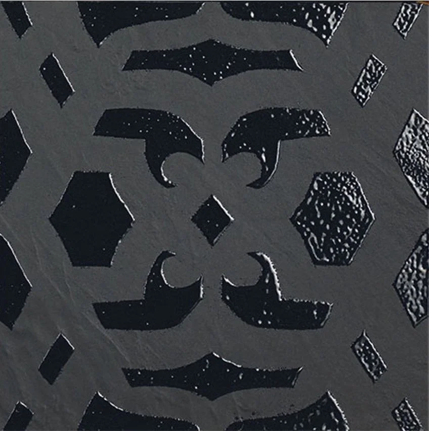 Close-up of a decorative metal window with geometric cut-outs, including hexagons, diamonds, and other shapes, with a dark background visible through the openings.