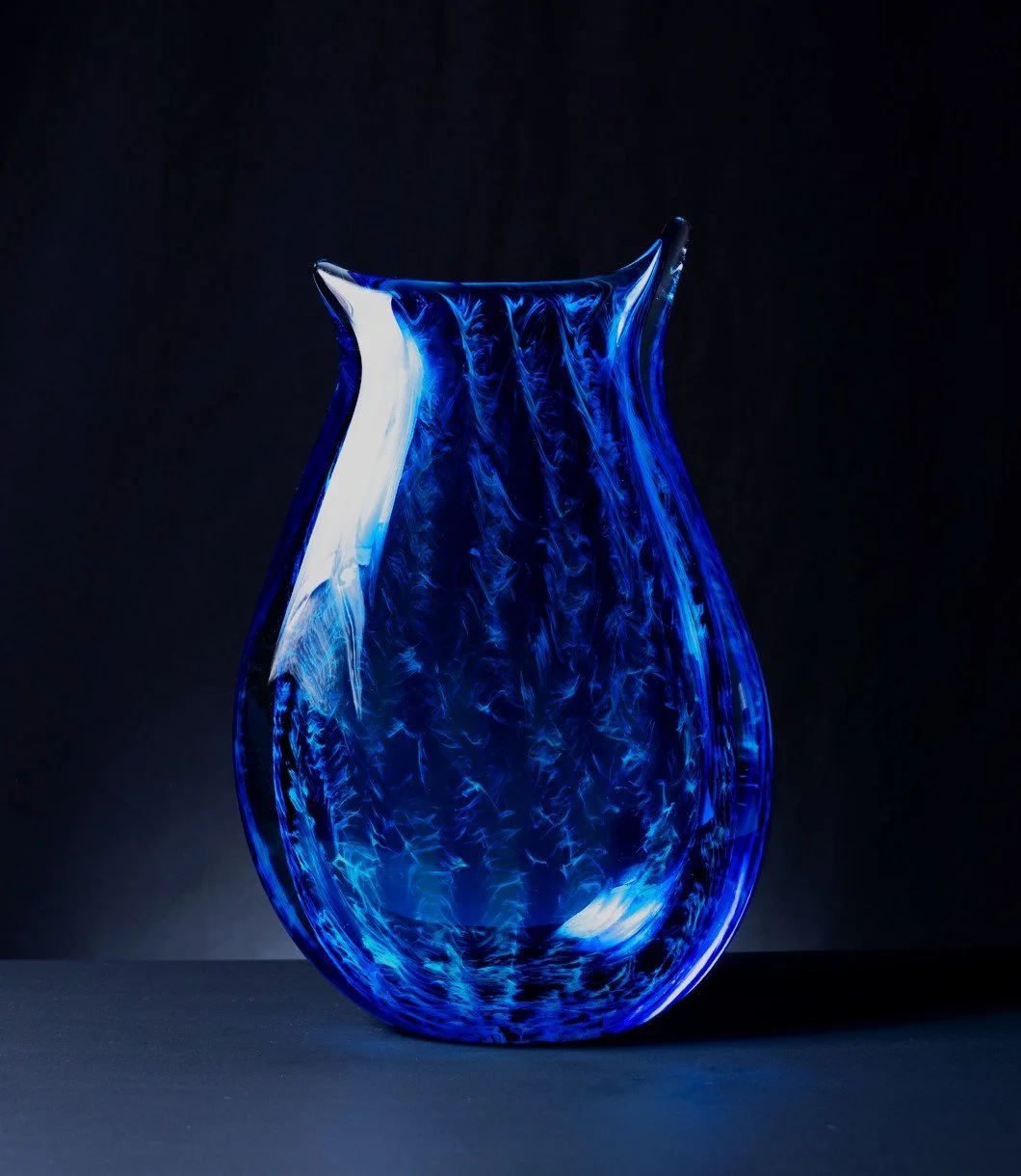 A blue glass vase with swirling patterns is displayed against a dark background.