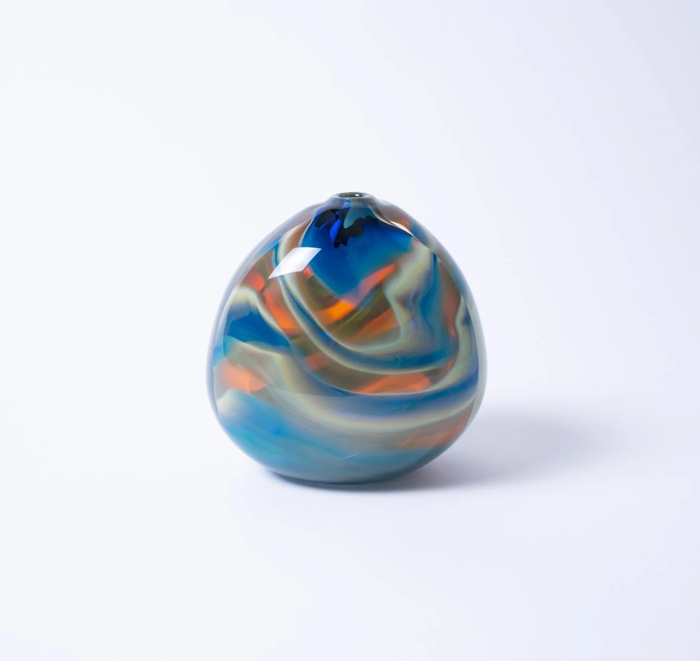 Colorful marbled glass ornament with swirls of blue, orange, and cream on a white background.