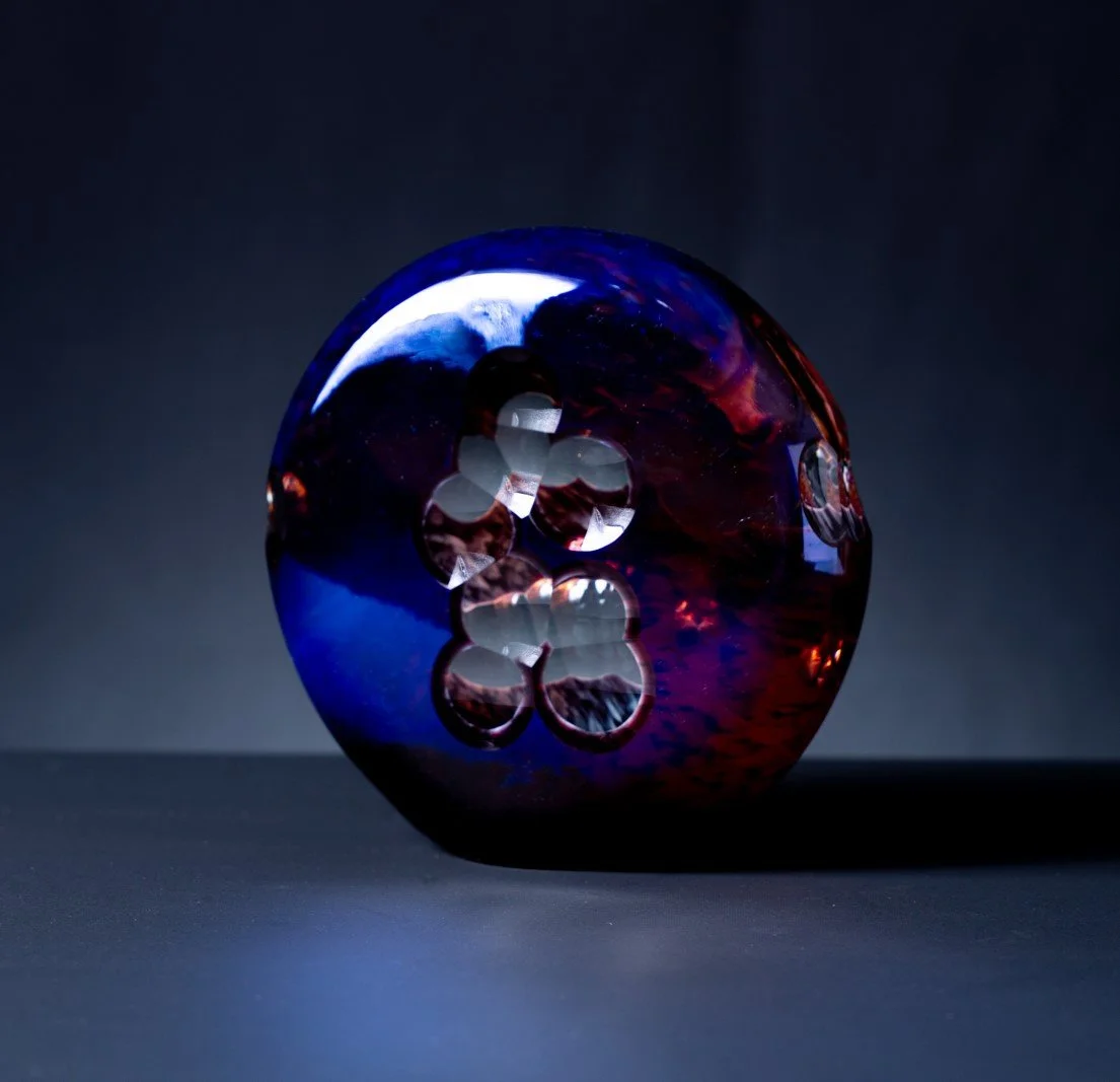 Colorful glass marble with swirls of blue, red, and black, reflecting light against a dark background.