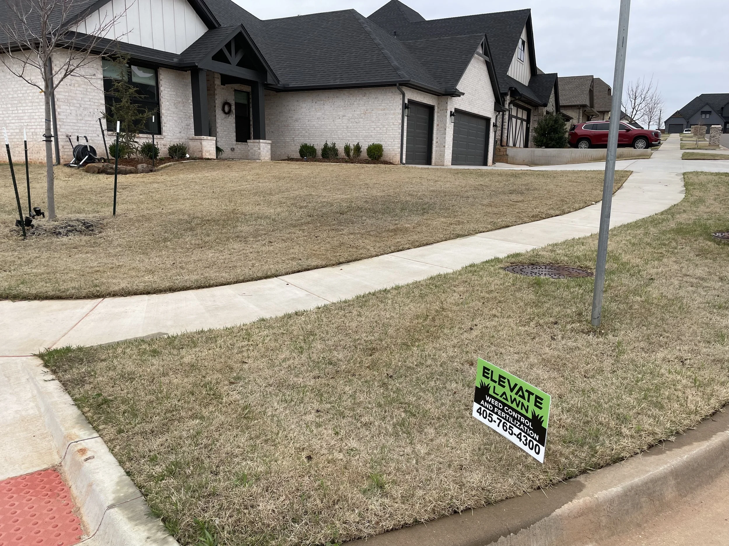 Suburban brick homes with manicured lawns, sidewalks, driveways, and a lawn weed-control service sign.