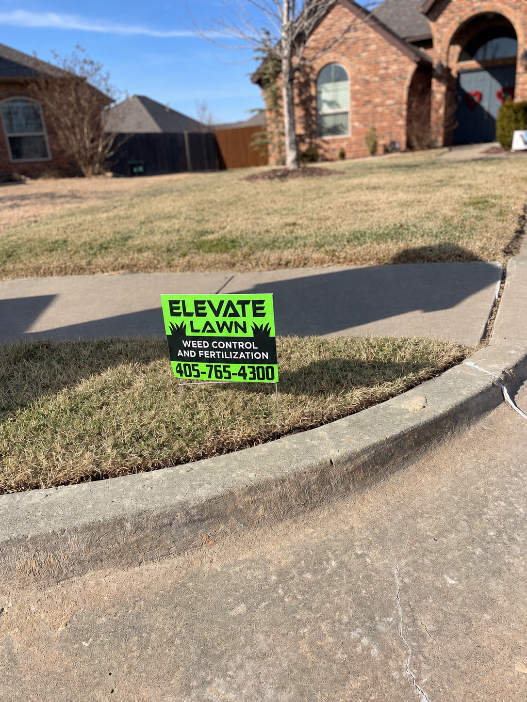 Bright green Elevate Lawn yard sign advertising weed control and fertilization with phone number 405-765-4300.
