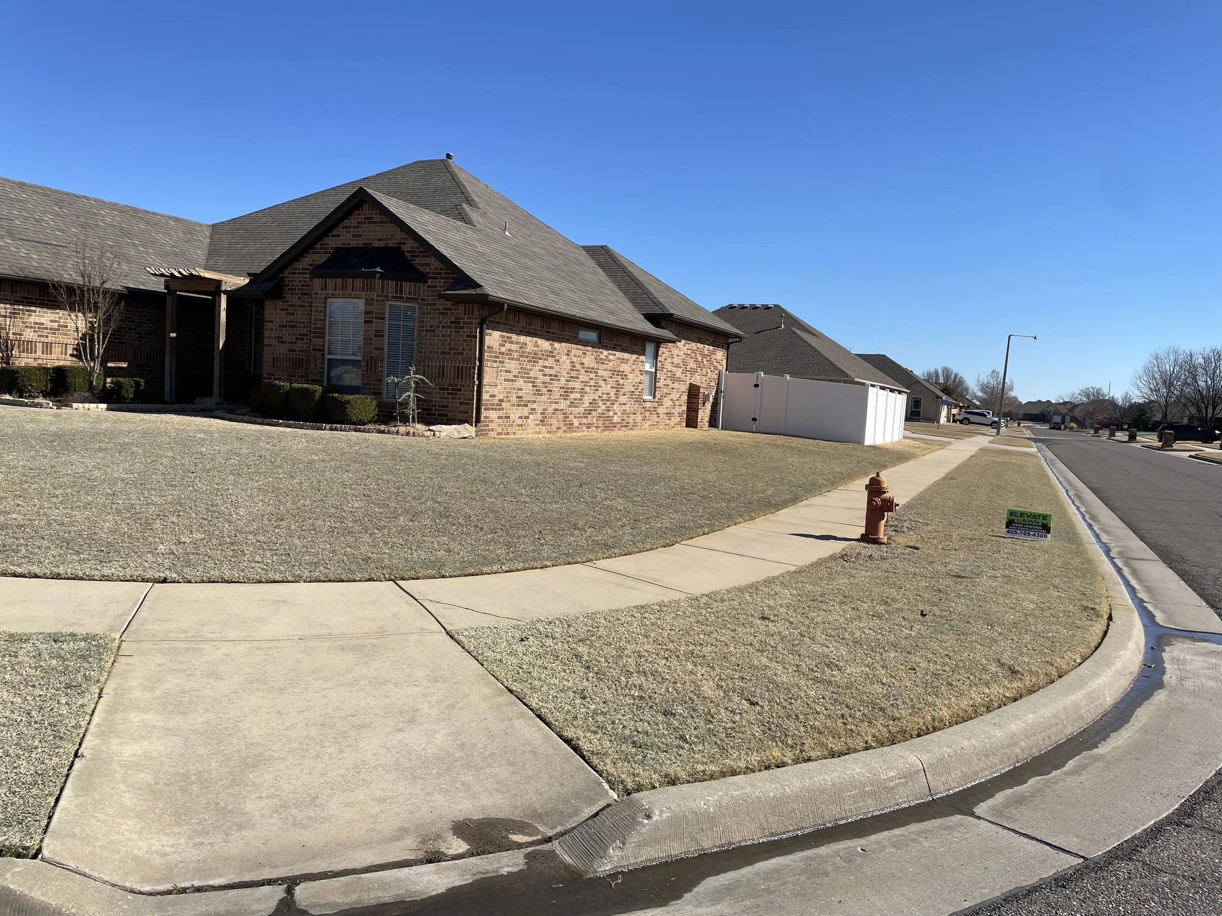 Brick suburban homes with manicured lawns, sidewalks, a fire hydrant, and residential street under a clear blue sky