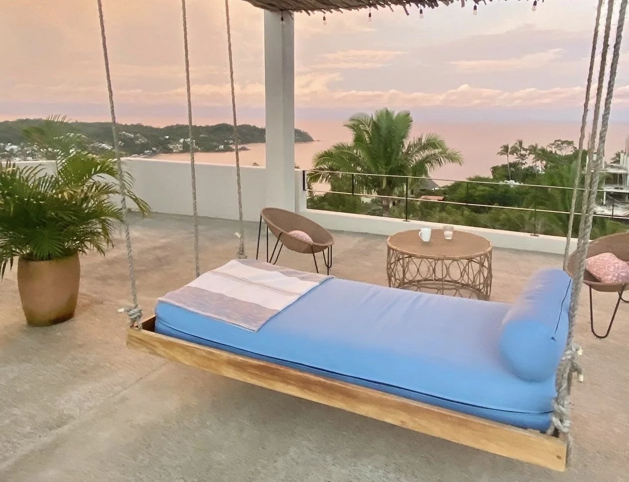 A bed swinging on ropes on the rooftop that looks out over the ocean view