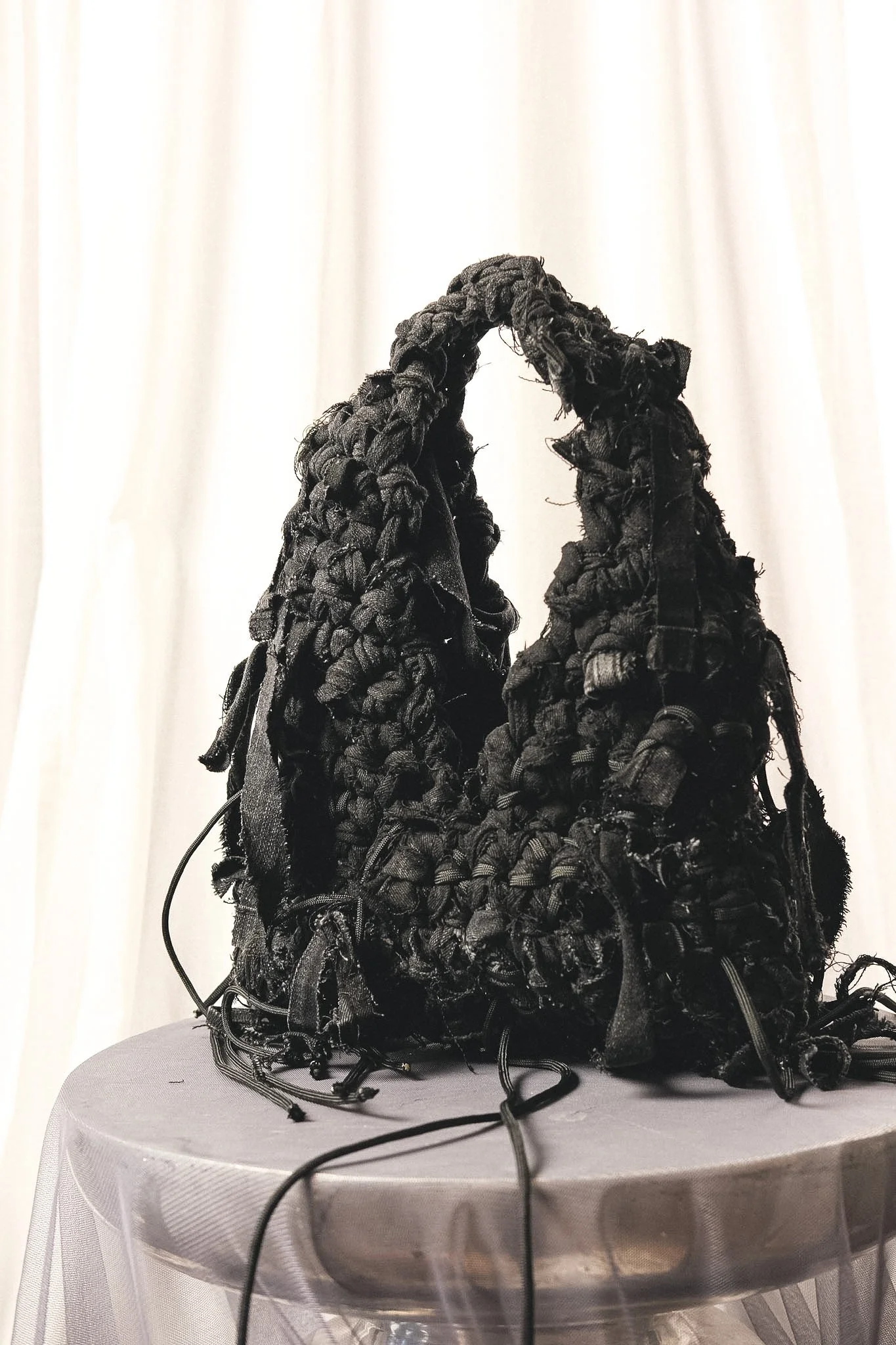 A sculptural denim bag made from black, textured fabric strips.