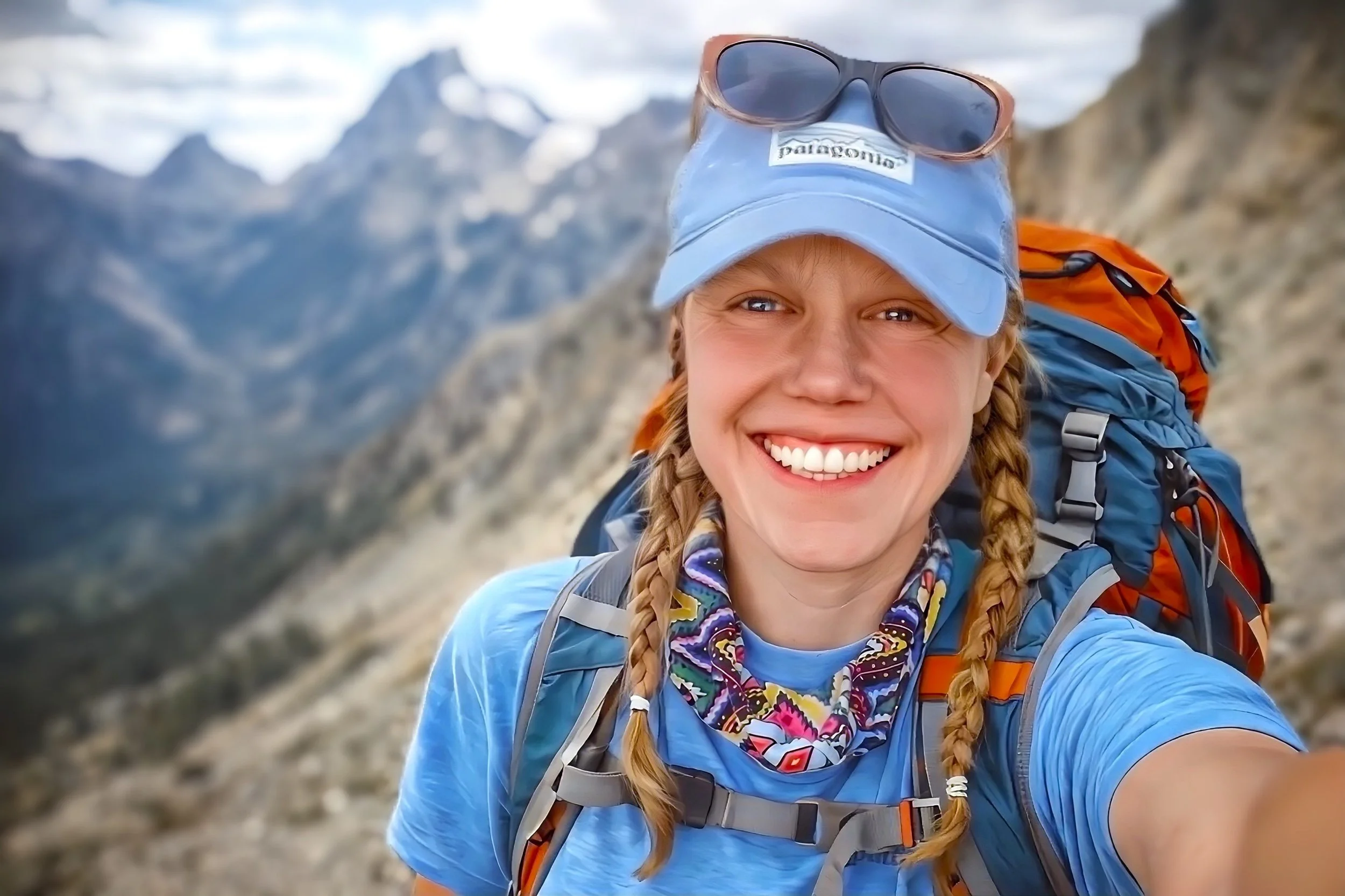 Sierra Summit Expeditions guide smiling on trail wearing a backpack and carrying safety gear, supporting Sierra Summit Foundation programs with trained outdoor leadership.