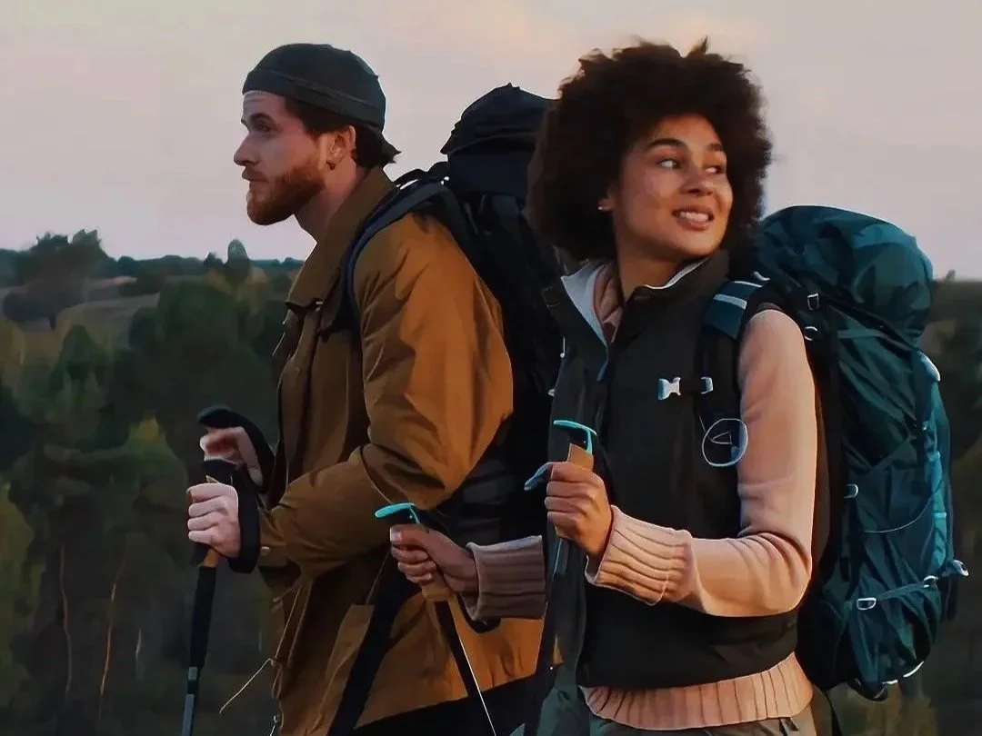 Two hikers with backpacks using trekking poles on a hillside at sunset, reflecting Sierra Summit Foundation’s mission to build strength, confidence, and belonging through outdoor access.