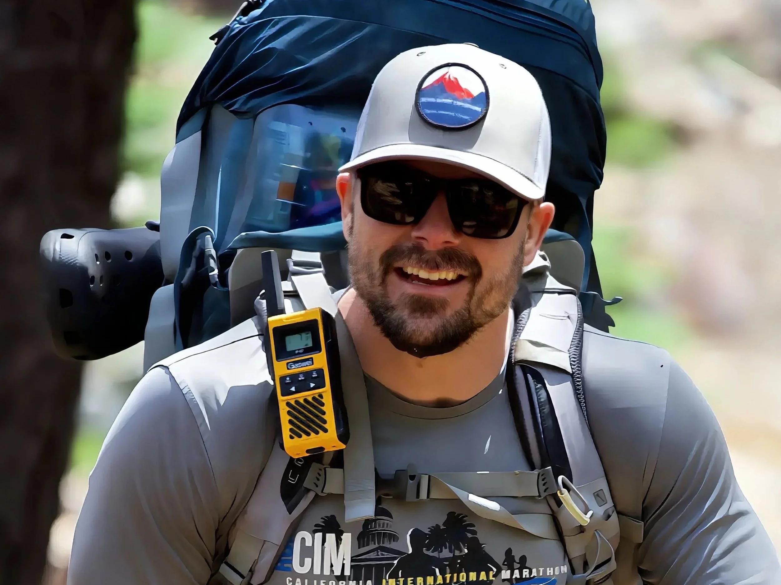 Sierra Summit Expeditions guide smiling on trail wearing a backpack and carrying safety gear, supporting Sierra Summit Foundation programs with trained outdoor leadership.