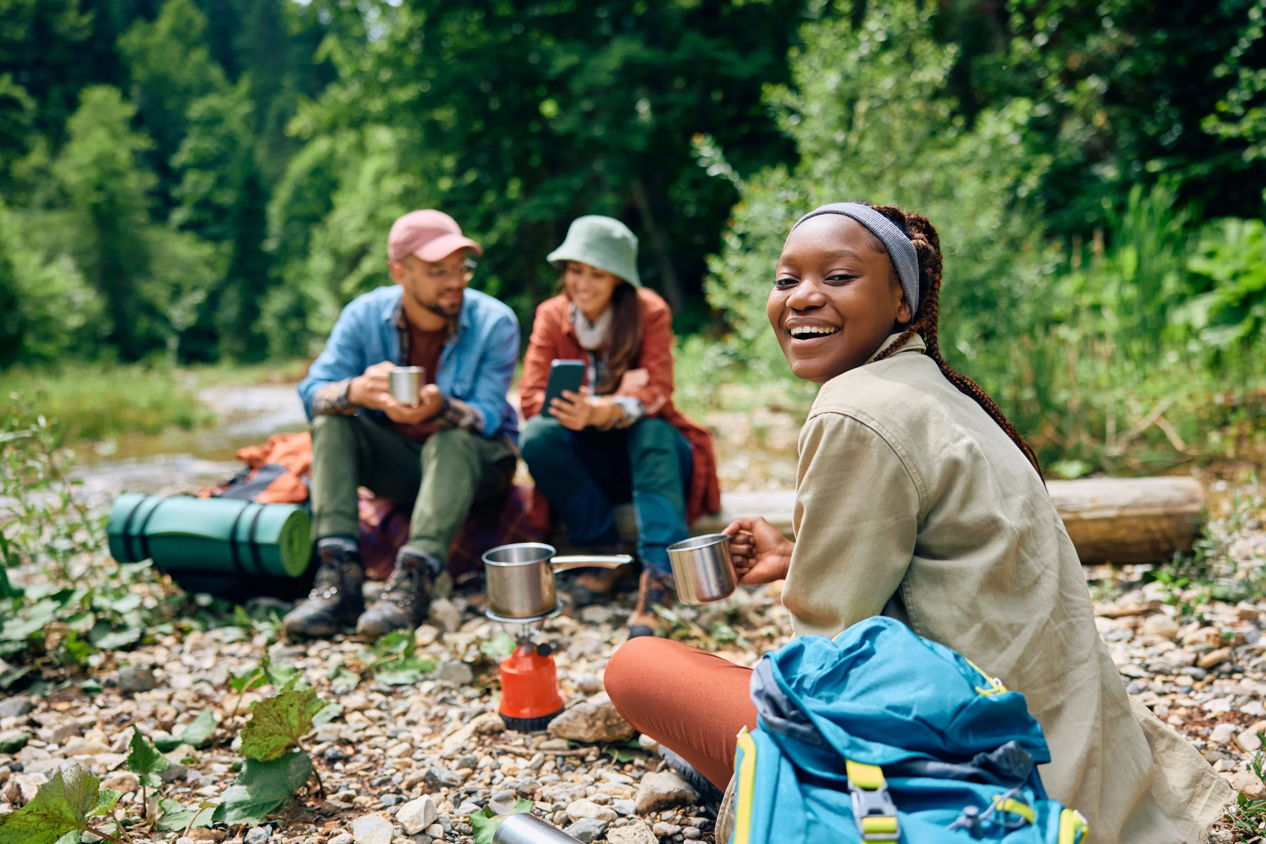 Young hikers taking a break by a creek and sharing a warm drink at camp, reflecting Sierra Summit Foundation’s mission to create belonging, confidence, and access to outdoor experiences.