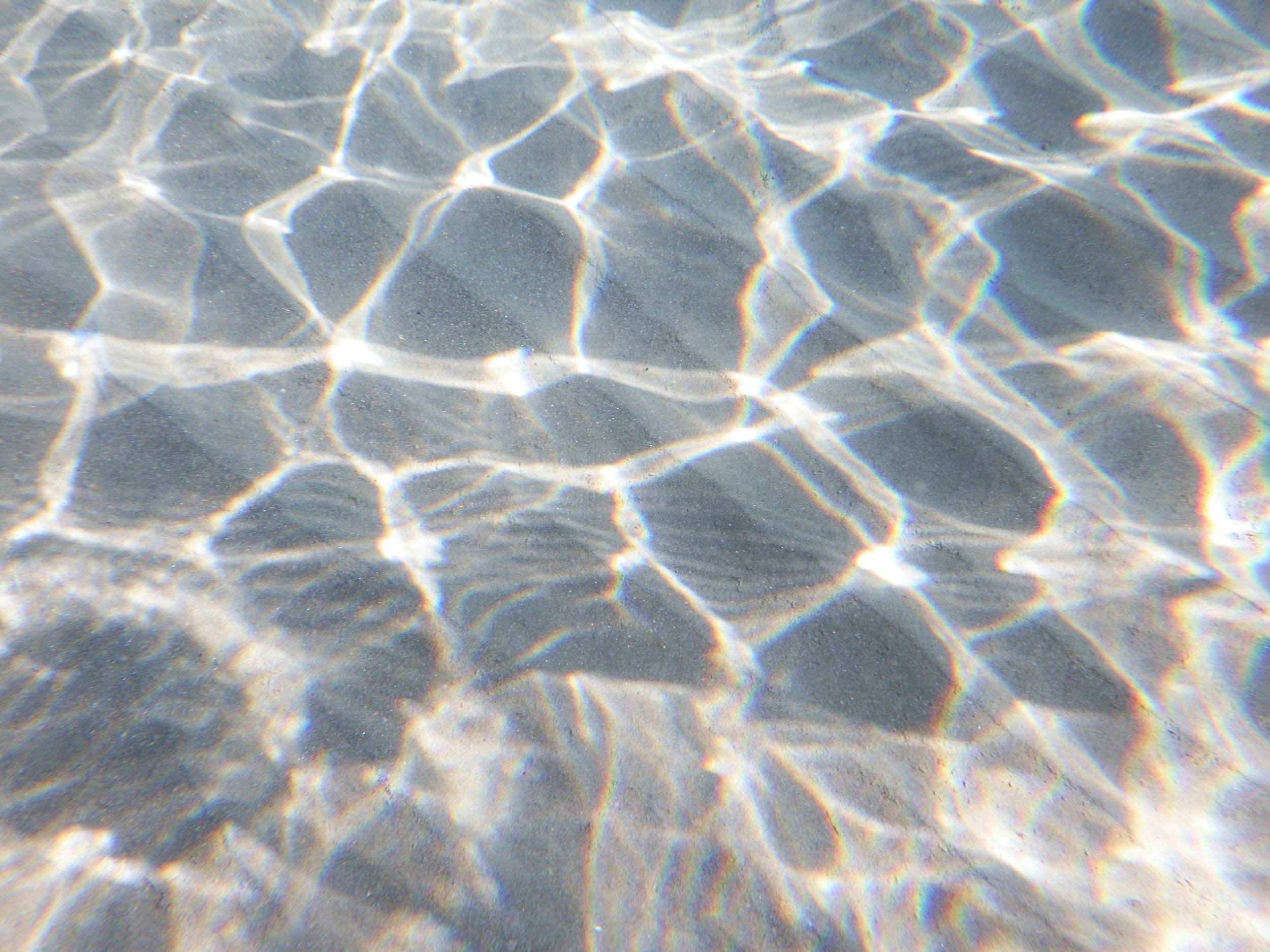 Sunlight reflecting on shallow water creating a pattern of bright lines on the sandy bottom.