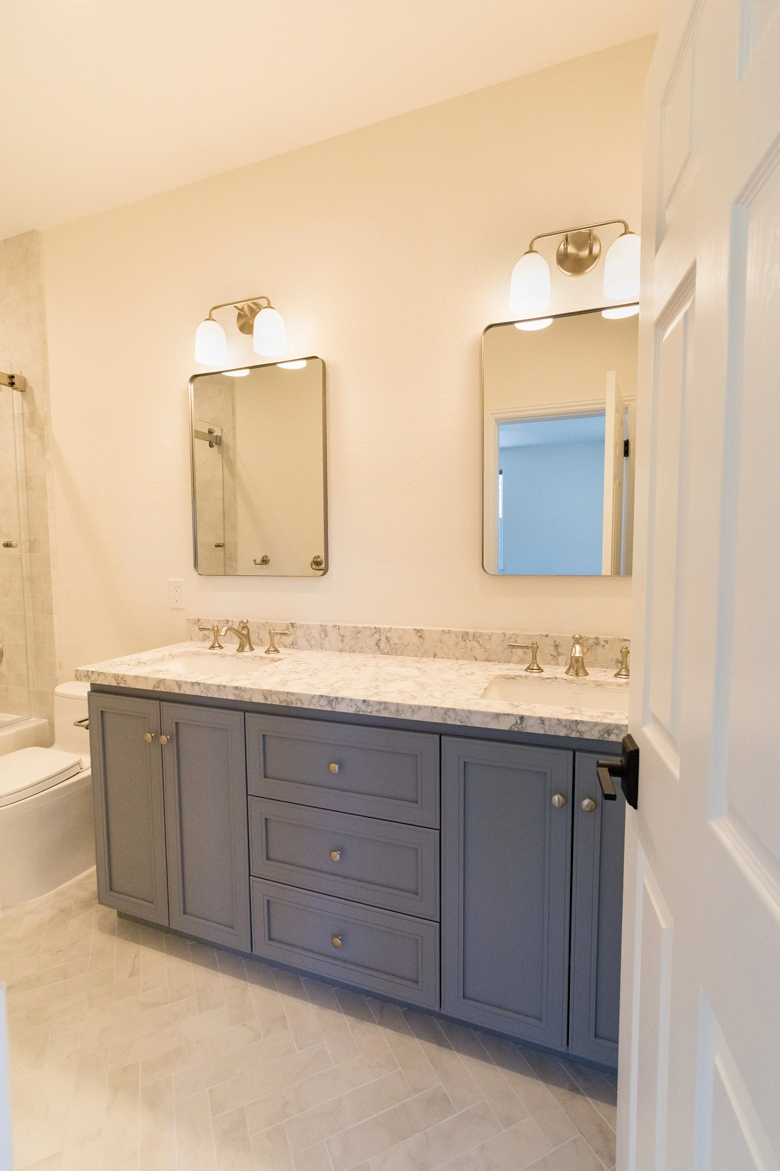 Bathroom with double vanity, marble countertop, two mirrors, and light fixtures.