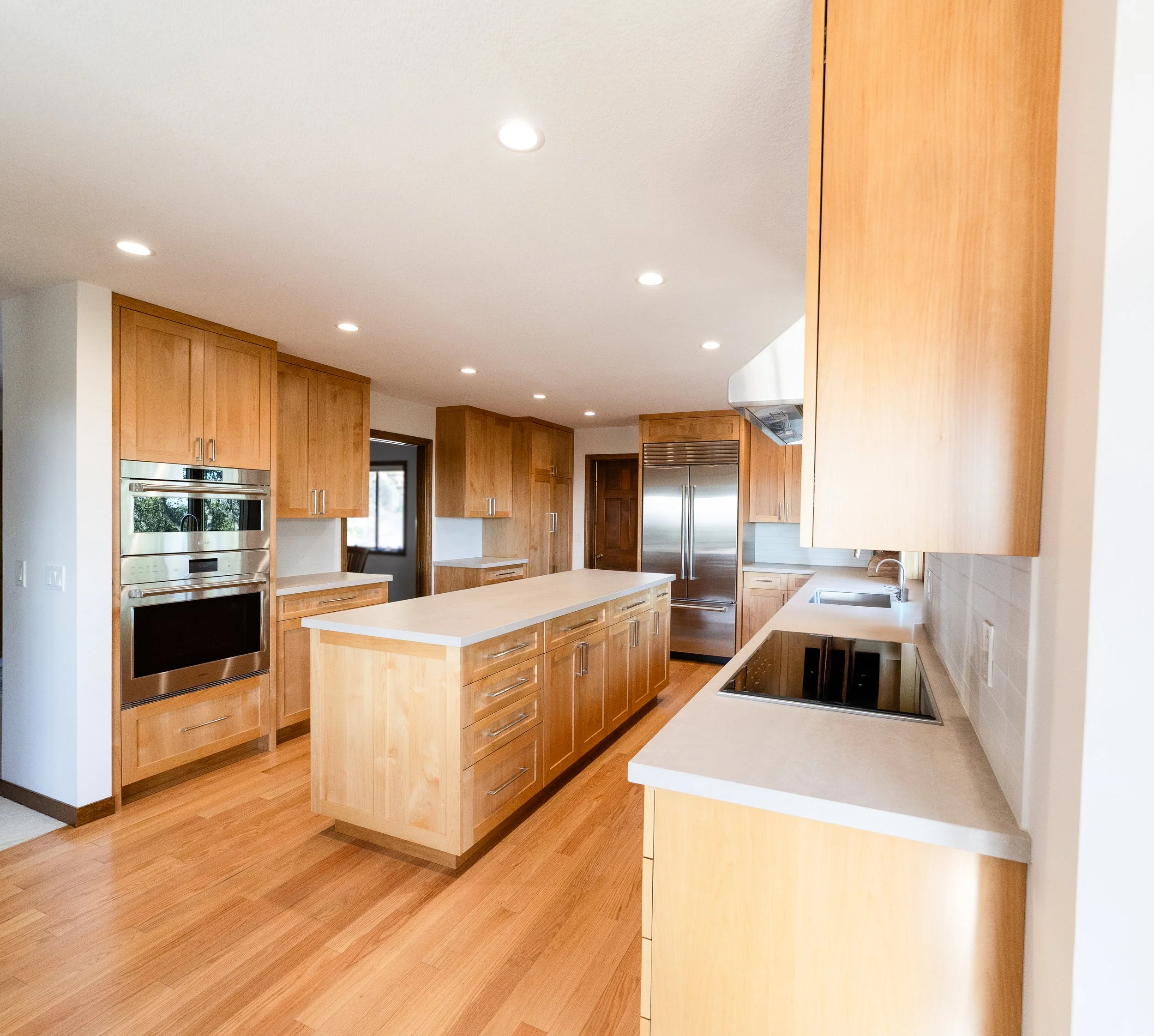 Photo of a modern kitchen with wooden cabinets, a kitchen island, and stainless steel appliances including a refrigerator and wall oven.