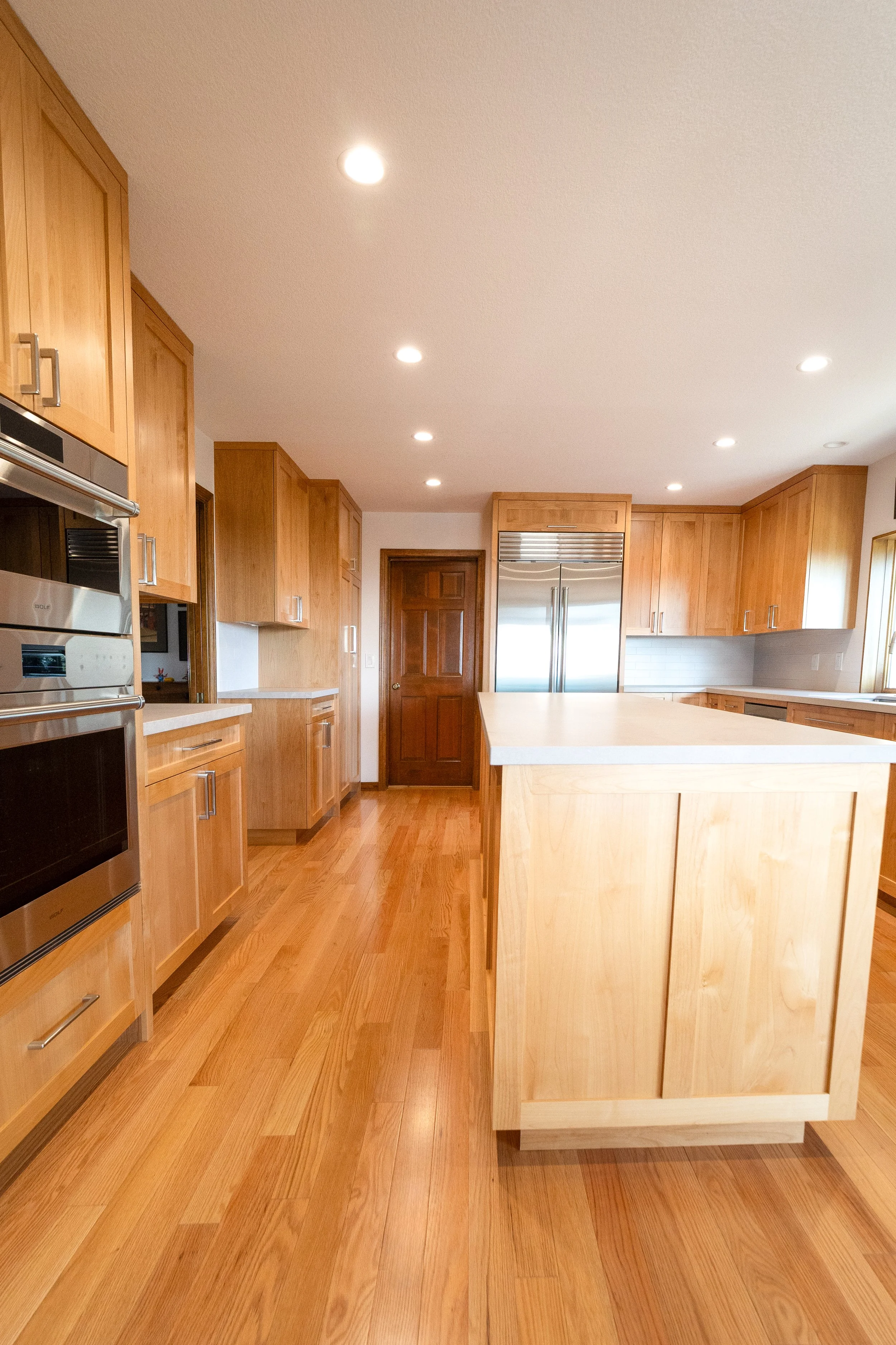 A spacious kitchen with wooden cabinets, hardwood flooring, a central island with a light-colored countertop, and stainless steel appliances.