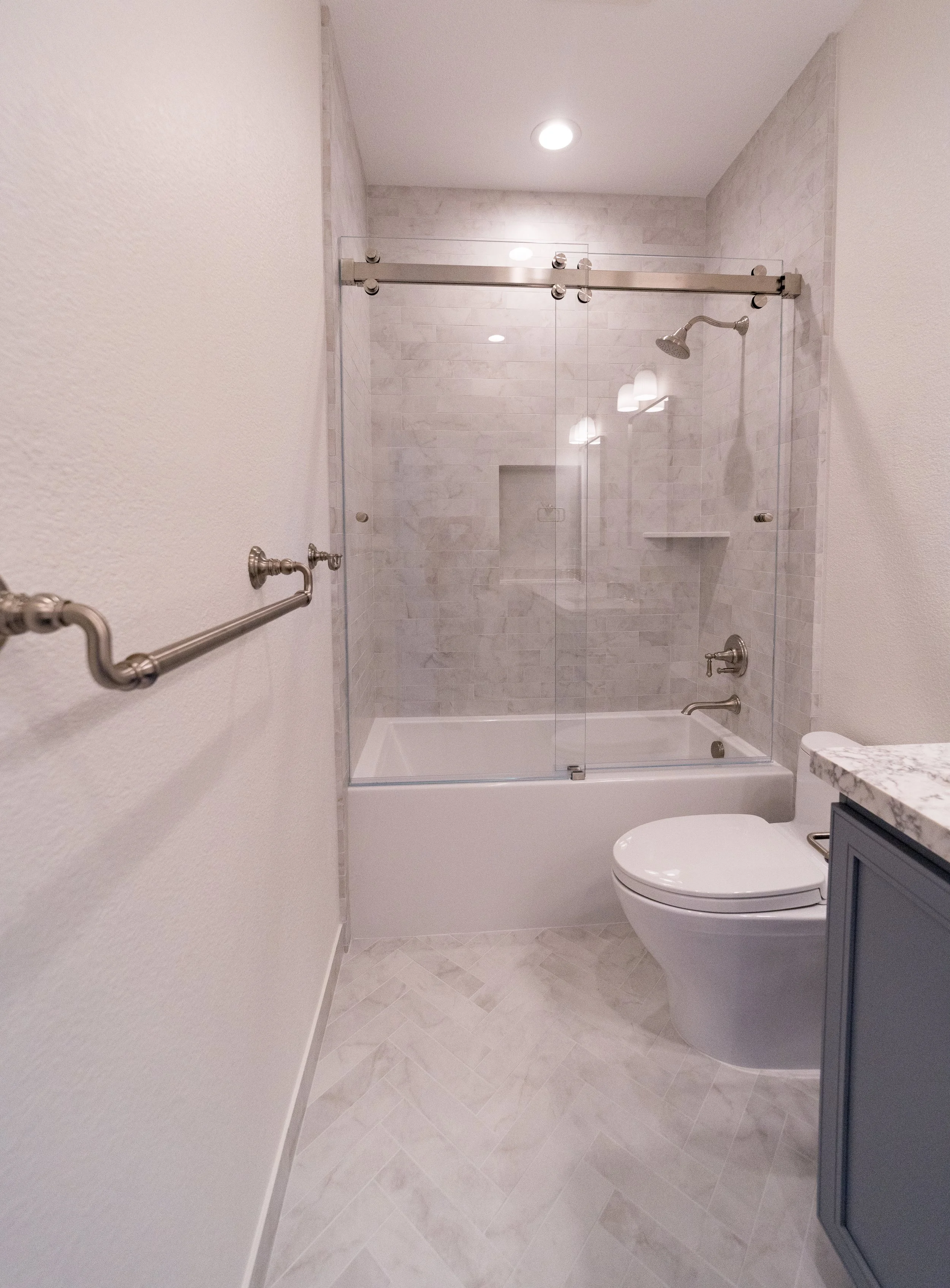 Modern bathroom with a walk-in shower with glass doors, shower fixtures, a bathtub, a white toilet, a granite countertop, and a blue cabinet.