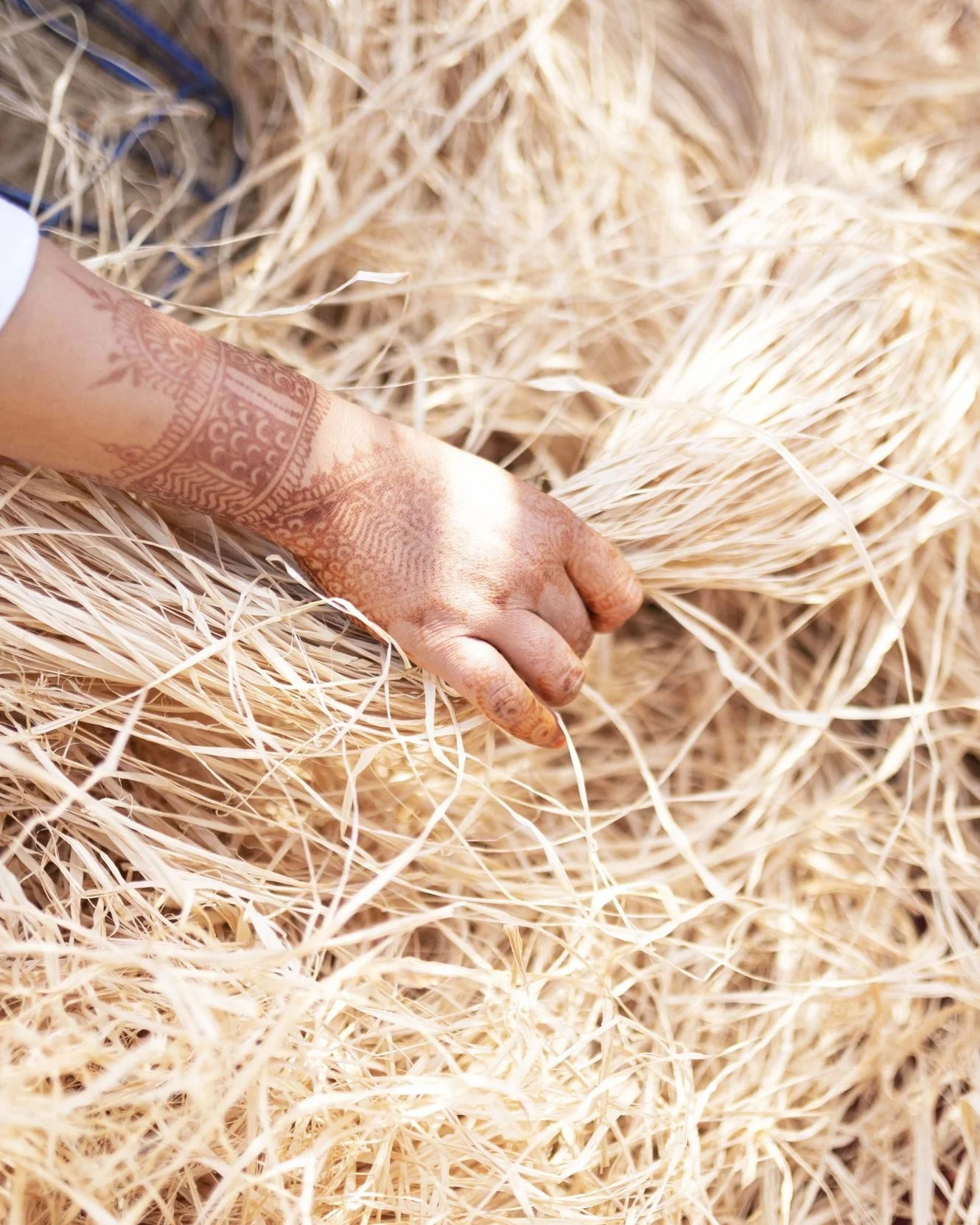 A hand with henna artwork resting on a bed of straw or dried grass.