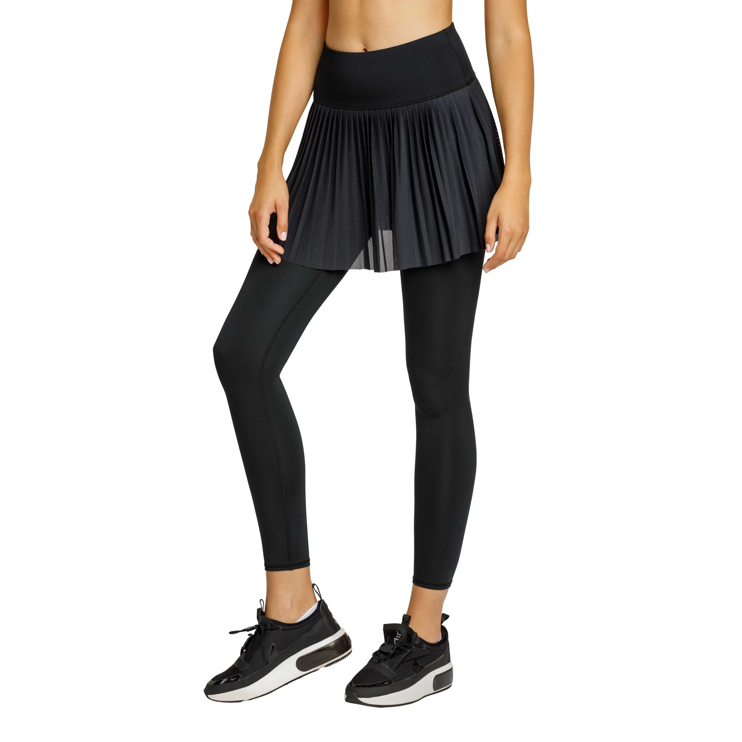A woman wearing black workout leggings, black sneakers, and a black pleated skirt, with her right hand hanging down.
