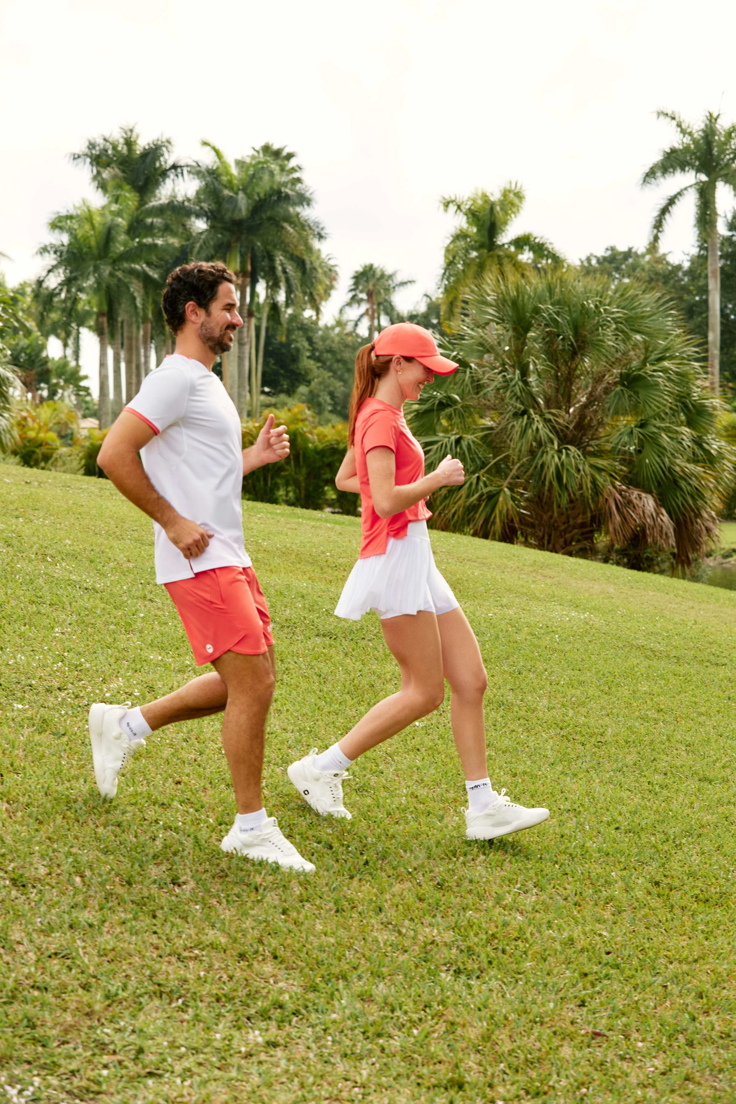 A man and woman jogging outdoors on a grassy area with palm trees in the background.