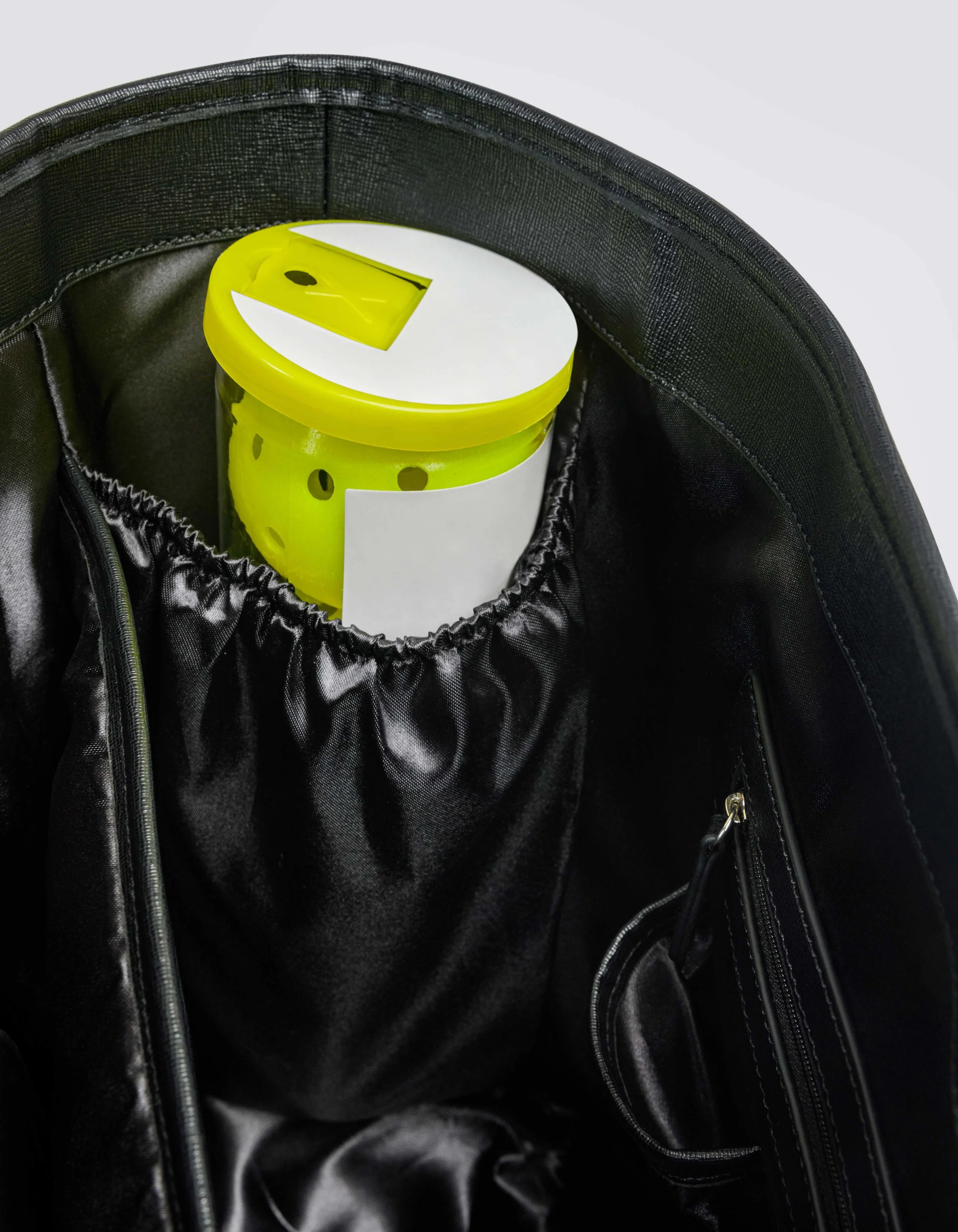 A black backpack with a padded interior pocket, holding a yellow plastic container with a white lid.