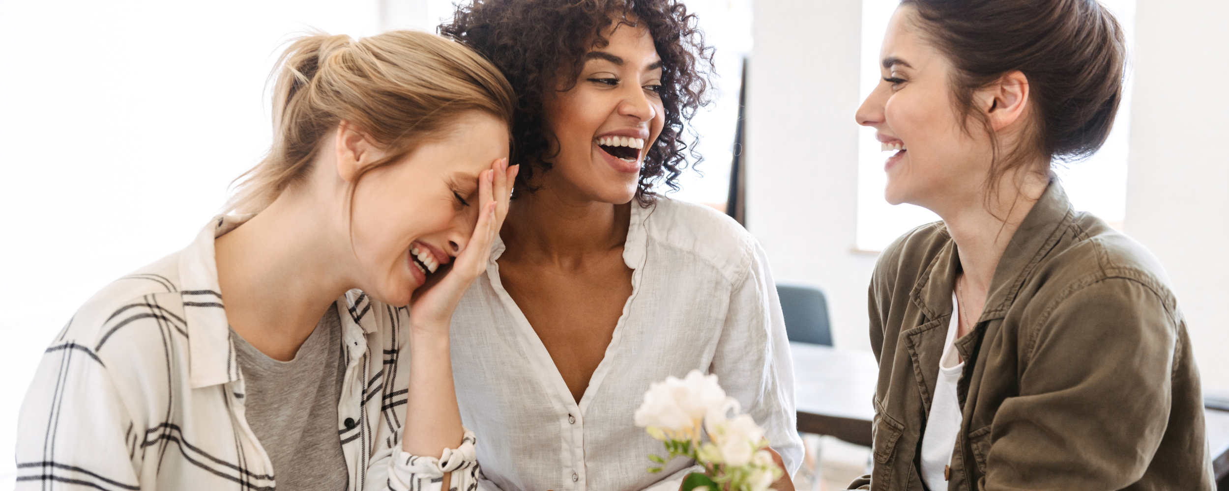 Three women laughing together, symbolizing support, friendship, and motherhood community.