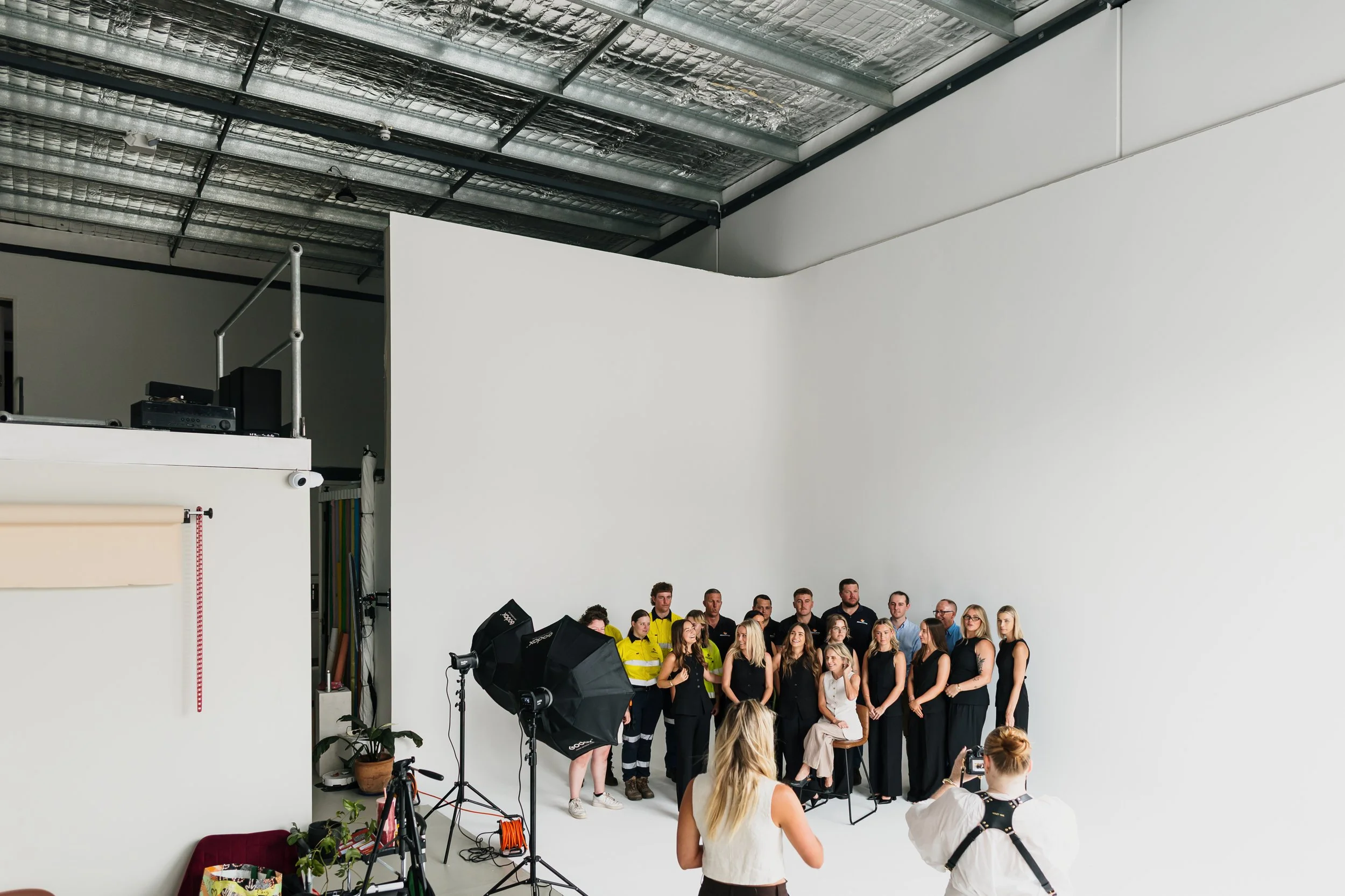 Group of people posing for a photo in a photography studio with a white background. There are professional lights and a photographer in the foreground taking the picture.