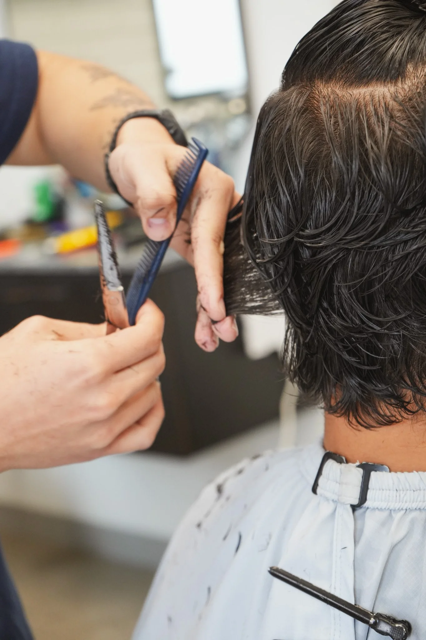 A hairstylist is cutting a person's hair with scissors and a comb in a salon.