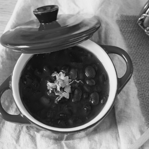 Feijão preto com caldo servido em uma panela de cerâmica vermelha, representando uma refeição caseira com sabor brasileiro feita no exterior.