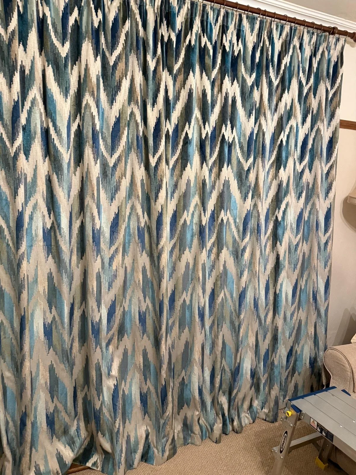A patterned curtain with zigzag design in shades of blue, beige, and black hanging from a curtain rod in a room.