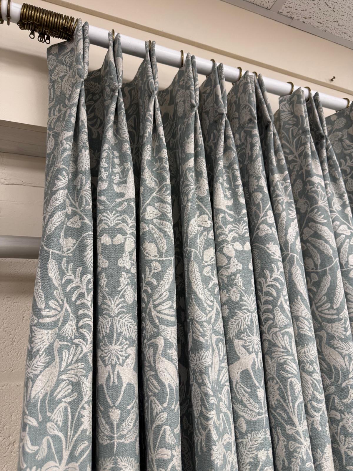 Blue and white patterned curtains hanging on a metal rod in an indoor setting.