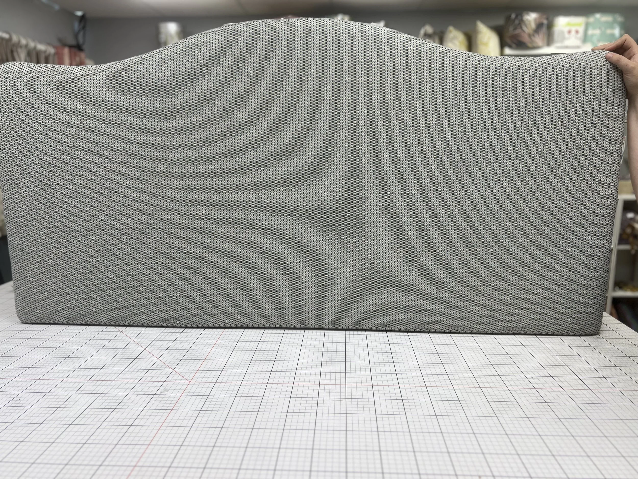 A person holding a gray textured headboard in a store behind a cutting mat with a grid pattern.