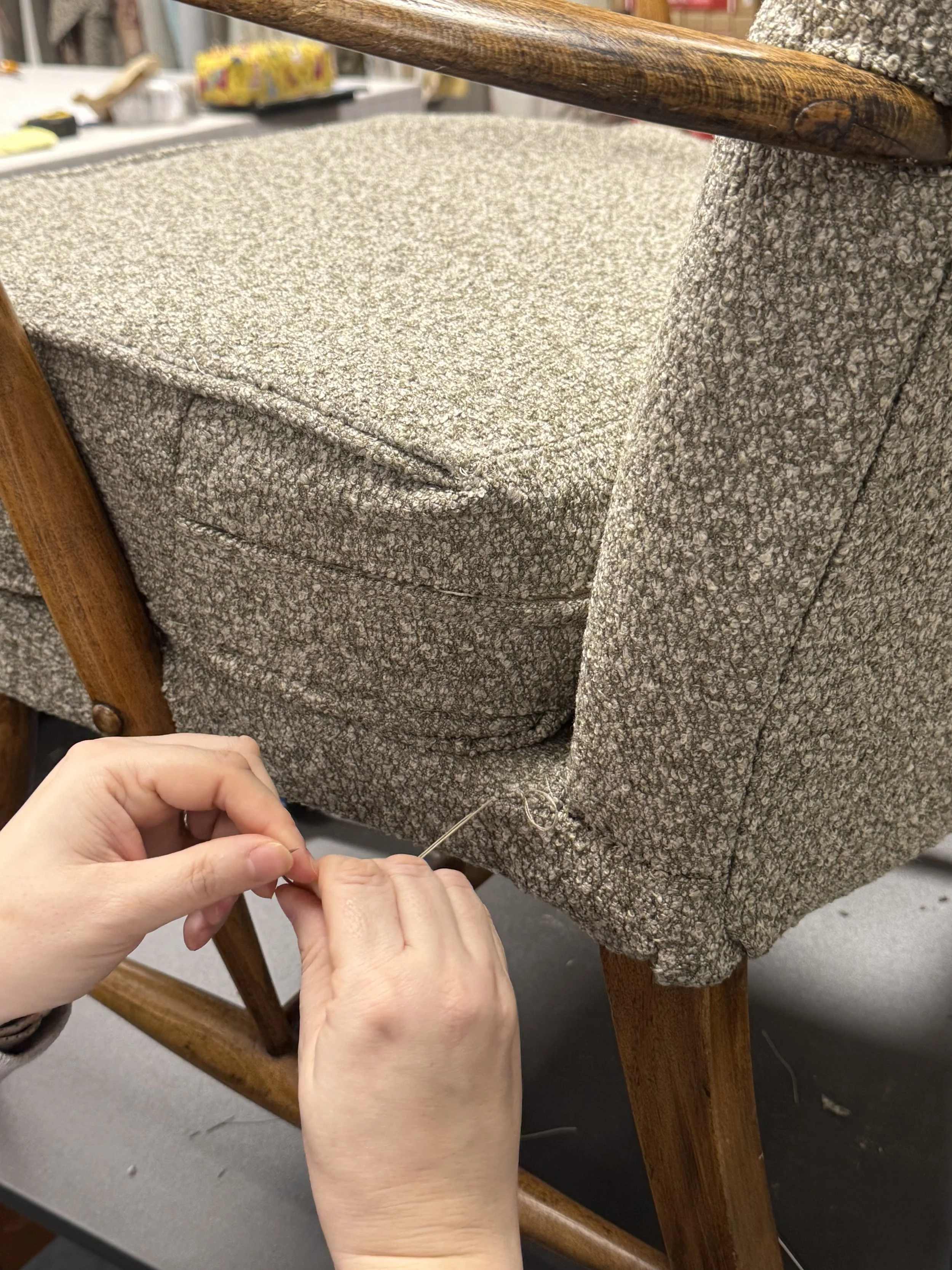 A person sewing upholstery fabric on a chair with wooden legs.