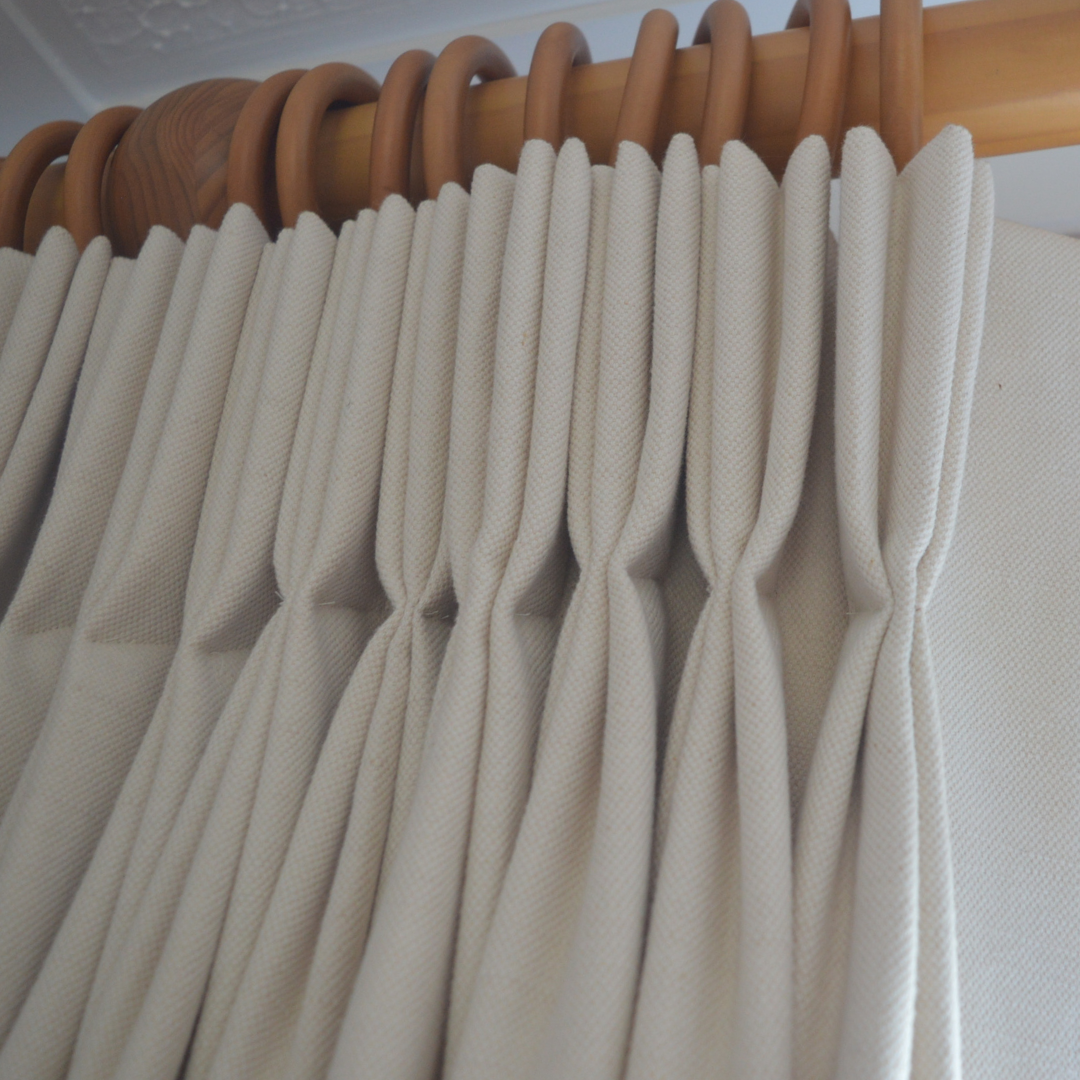 Close-up of beige curtains hanging on a wooden curtain rod.