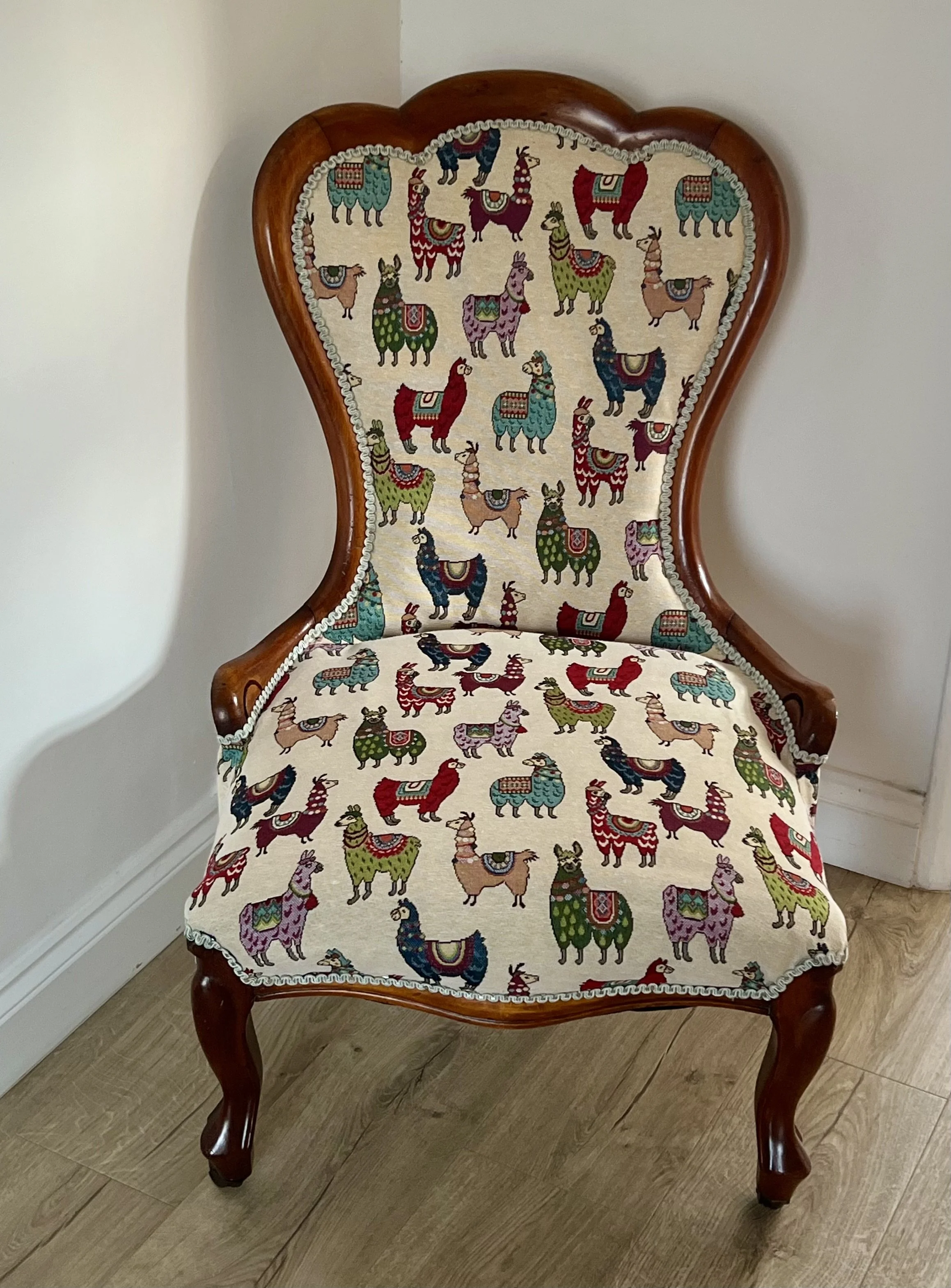 Vintage wooden chair with upholstery featuring colorful llama patterns, against a plain white wall.
