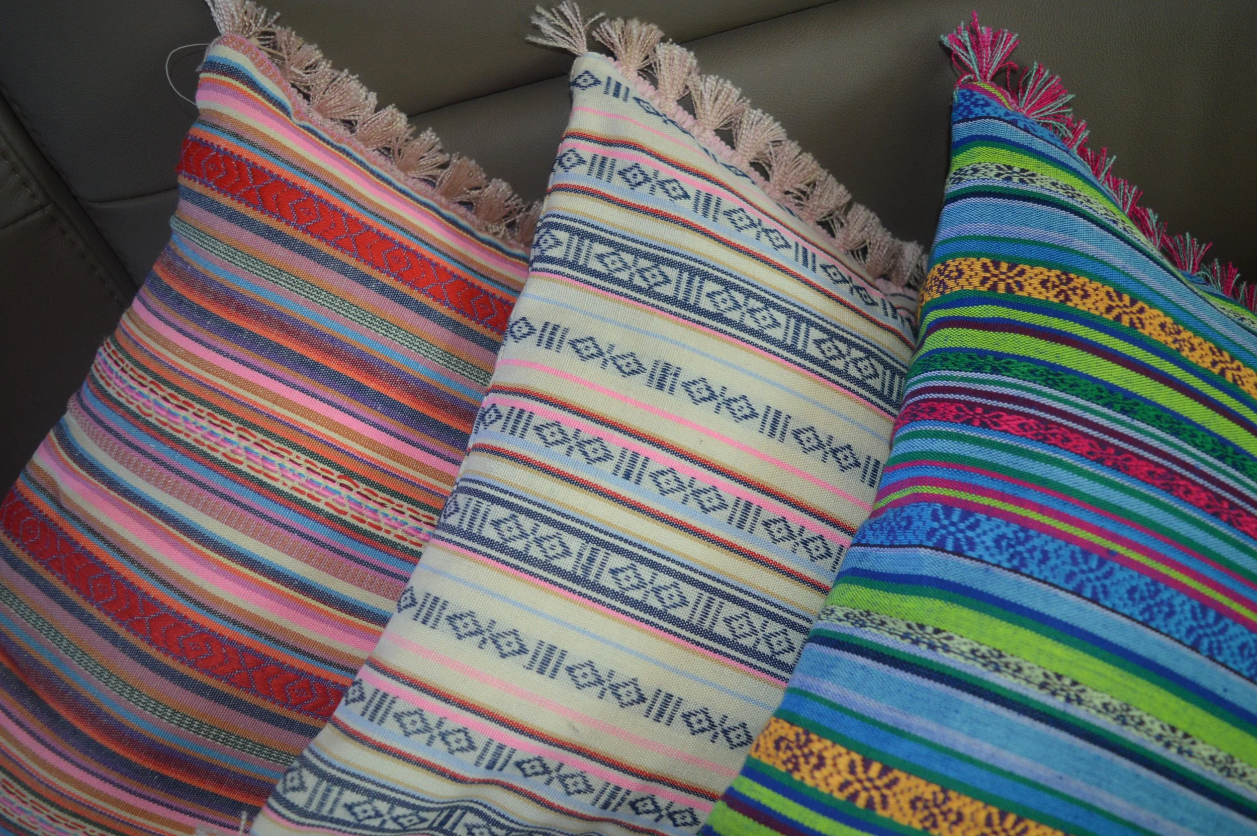 Three colorful woven decorative pillows on a couch, each with intricate patterns and fringed edges.