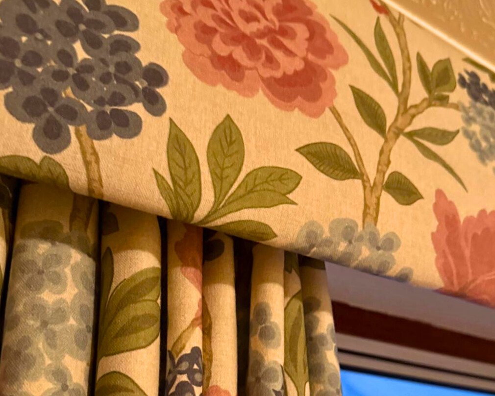 Close-up of floral-patterned curtains with a matching tablecloth featuring large pink, blue, and green flowers and leaves.